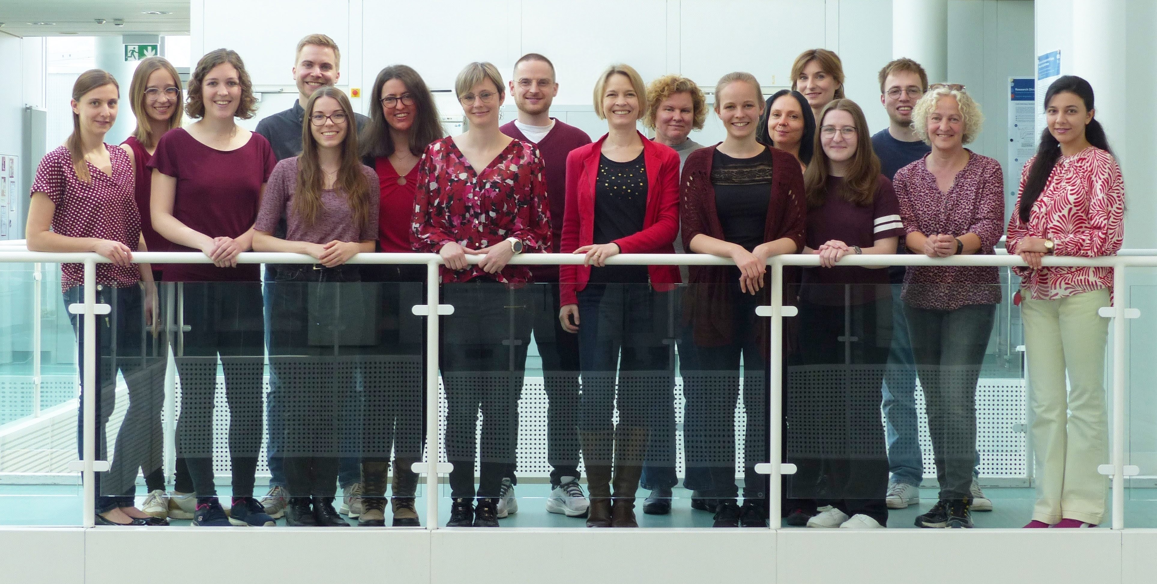 Sixteen members of the working group are standing behind a railing in a corridor in the DKFZ building.