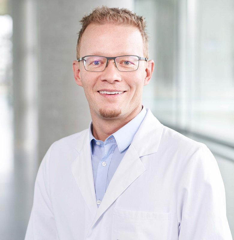 Smiling man with glasses, shirt and white coat