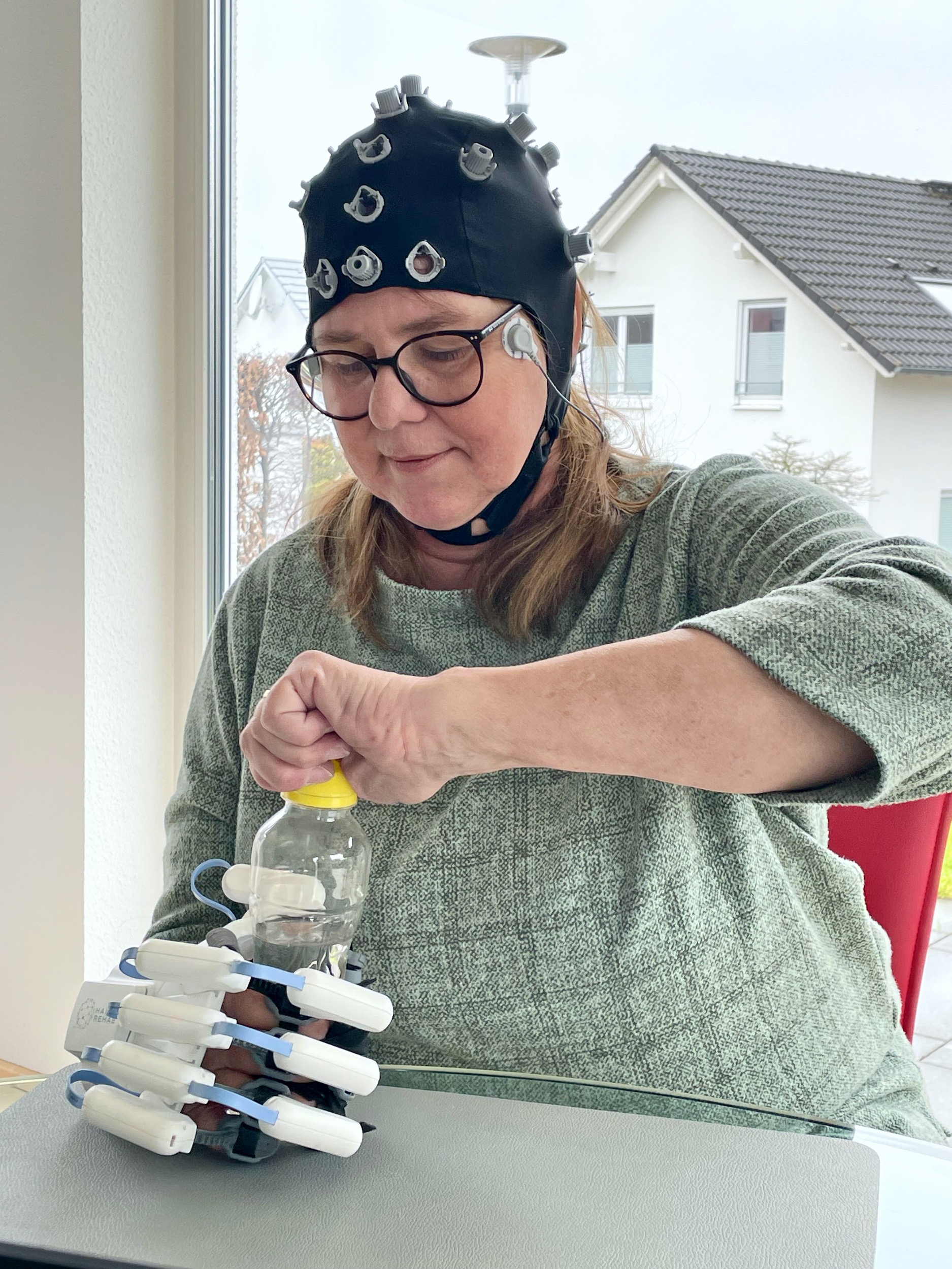 The photo shows a woman with an exoskeleton hand holding a plastic bottle.