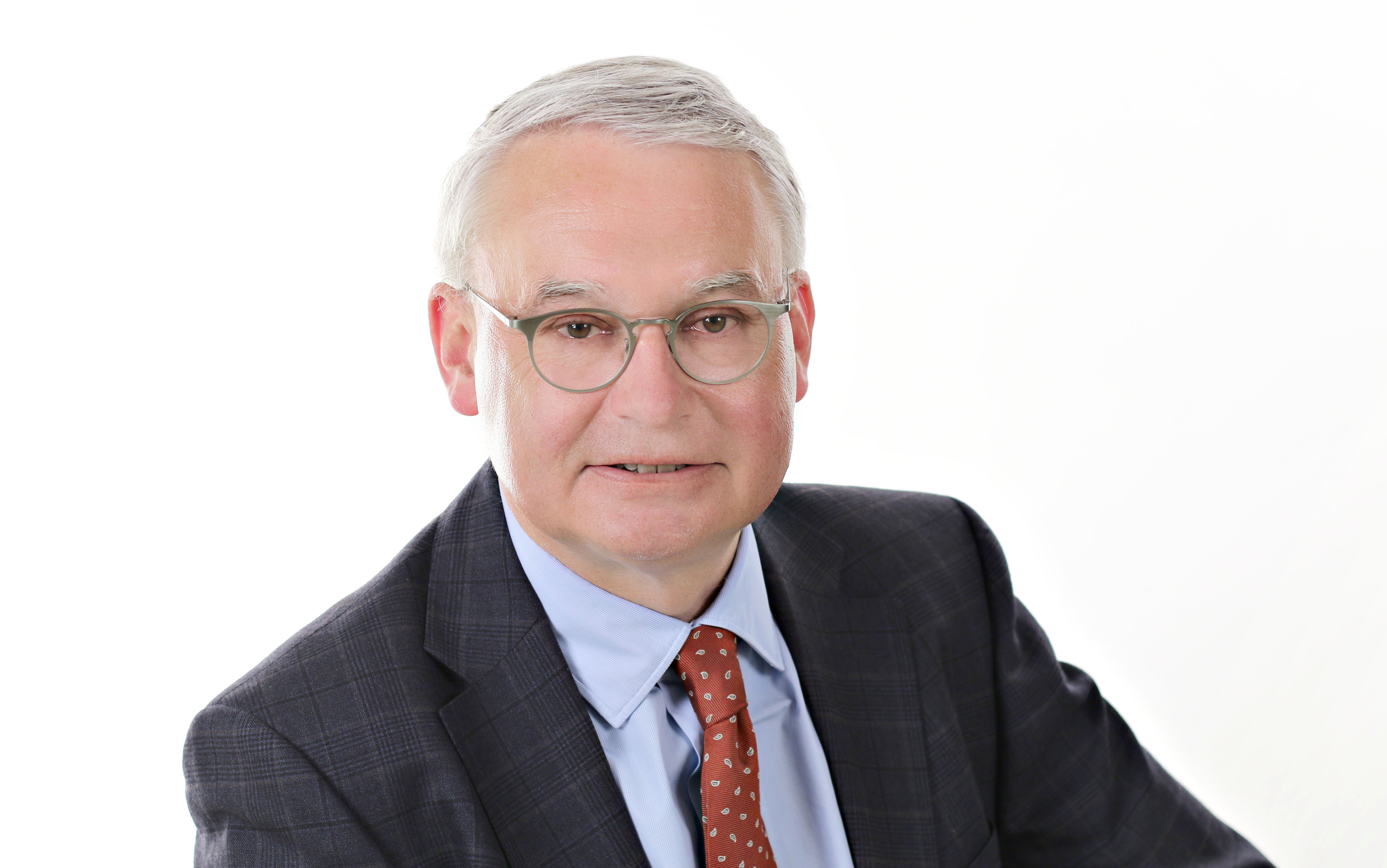 Portrait photo of friendly smiling man with short gray hair and glasses wearing a suit.