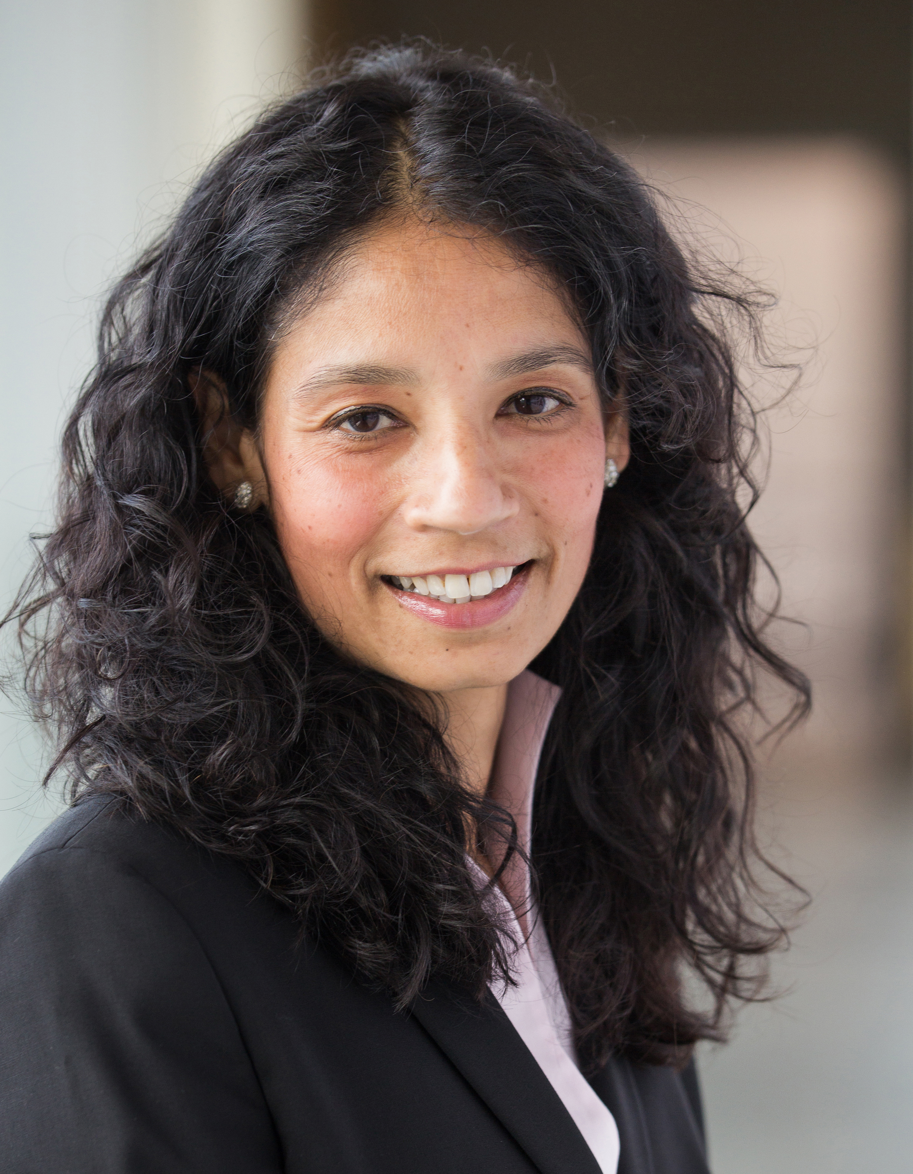 Portrait of a friendly smiling woman with long dark and slightly curly hair.