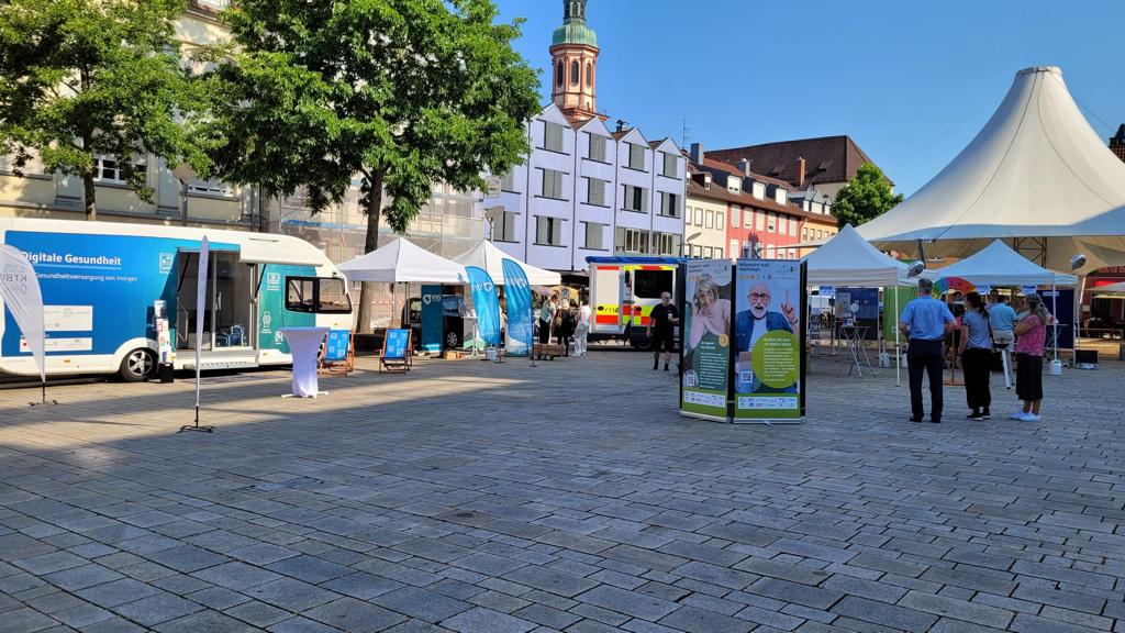 Der Truck steht neben mehreren Ständen auf dem Marktplatz. Verschiedene Menschen schauen von weitem auf die Stände.