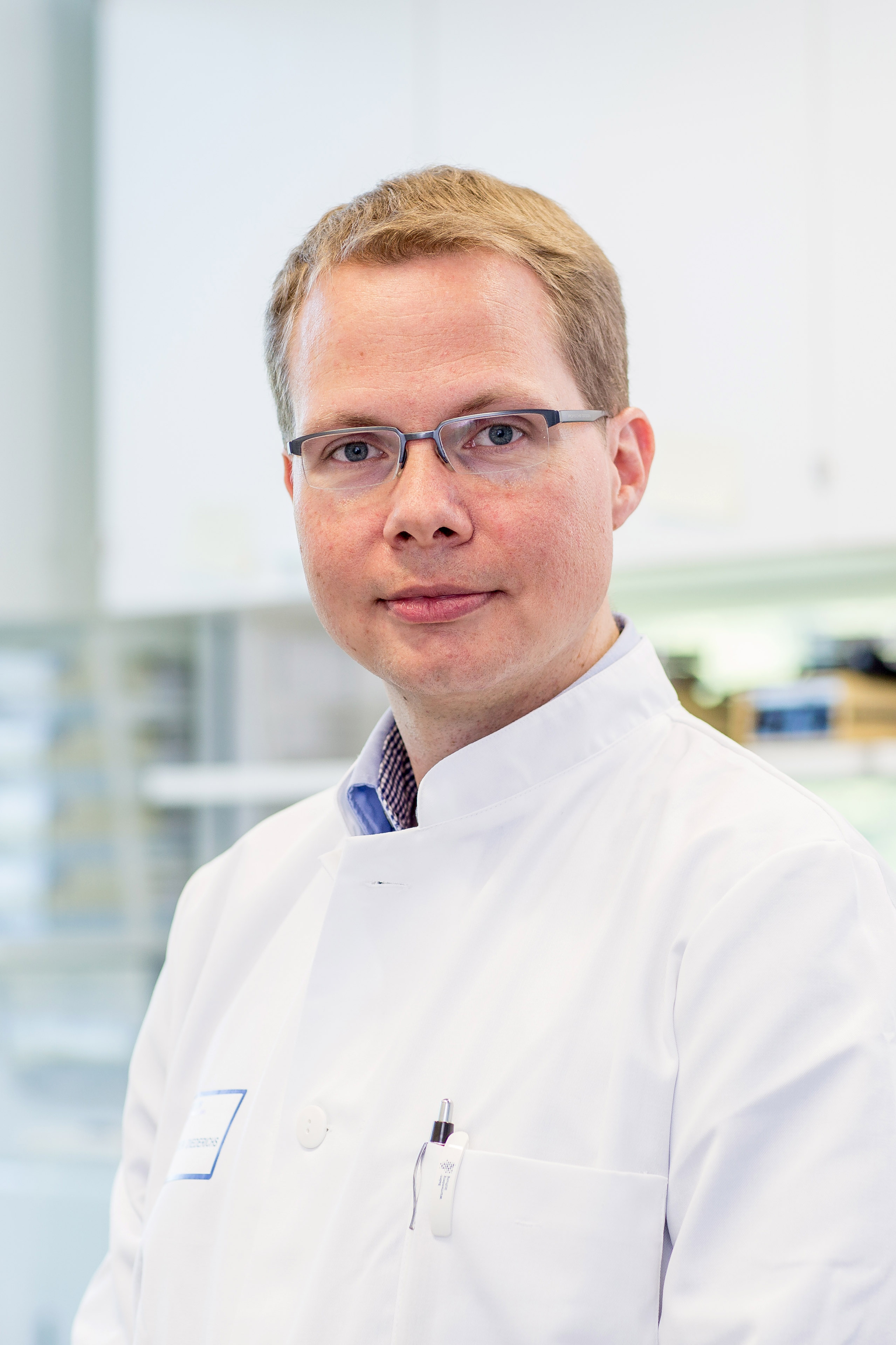 The photo shows a man in a laboratory coat smiling into the camera