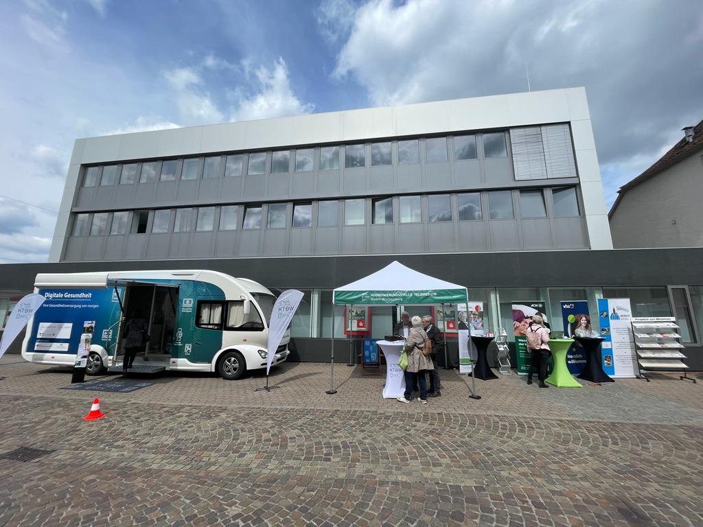 Der Truck steht neben verschiedenen anderen Ständen auf dem Marktplatz. Einige Besucher informieren sich.