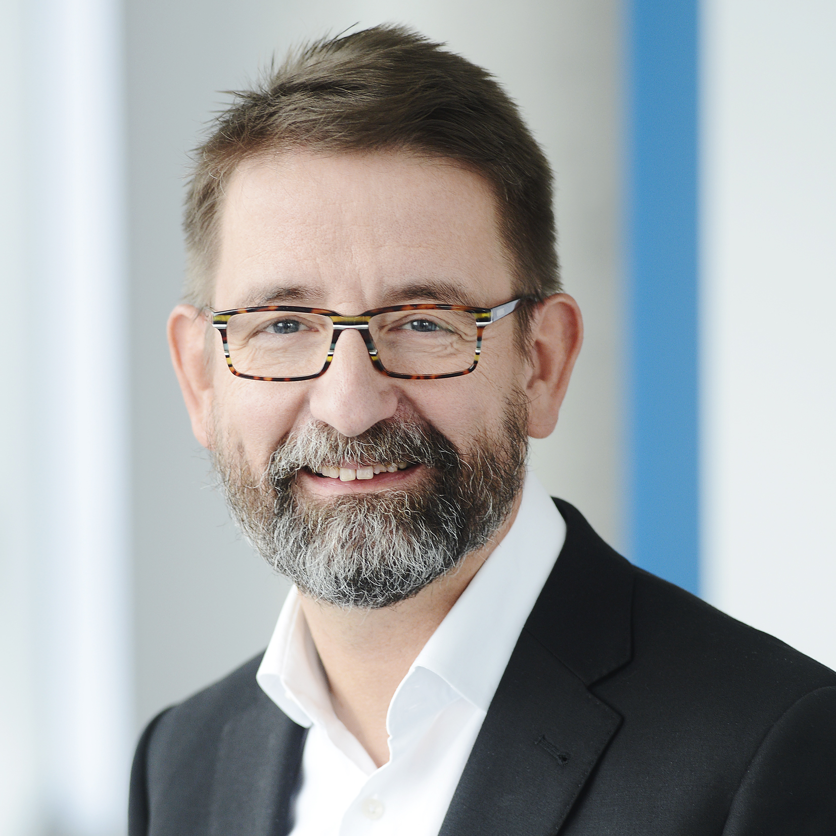 Portrait of friendly smiling middle-aged man with beard and glasses, wearing a suit.