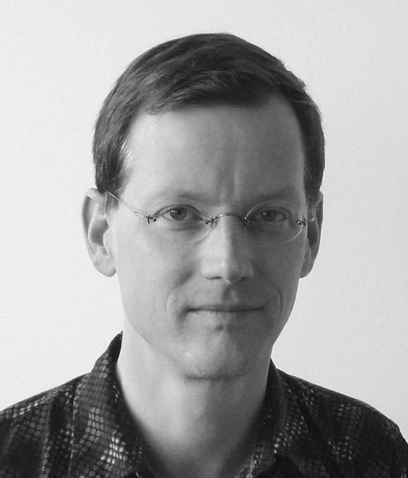 Schwarz-weiß Porträt eines Mannes mit kurzen Haaren und einer randlosen runden Brille.
