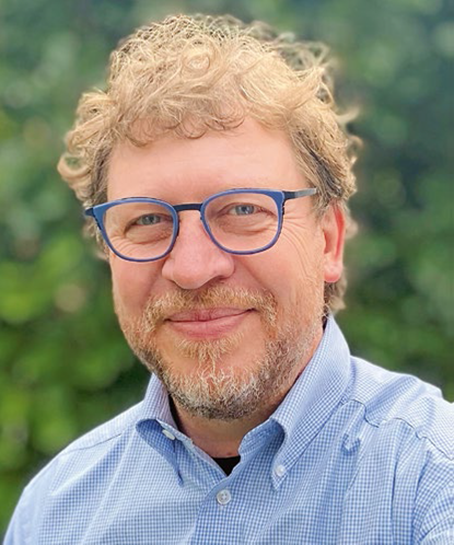 The image shows a man with blond hair and a beard smiling warmly at the camera.