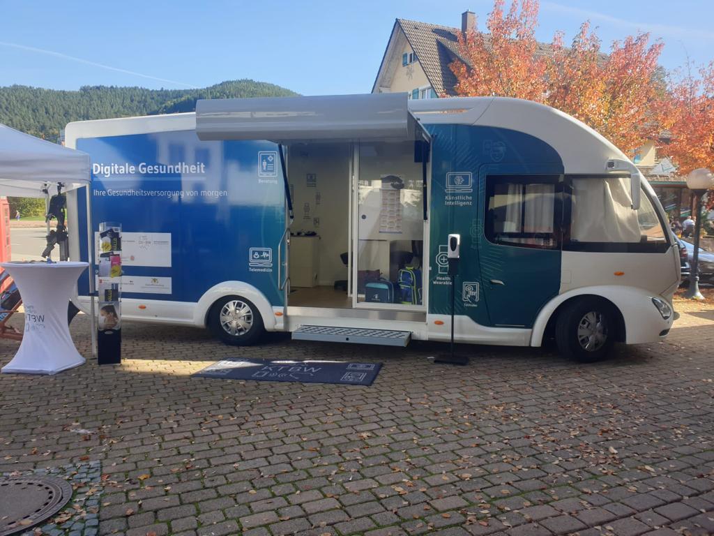 Der Truck steht bei blauem Himmel vor herbstgefärbten Bäumen. Im Eingangsbereich stehen Zeitschriften und Desinfektionsmittel.