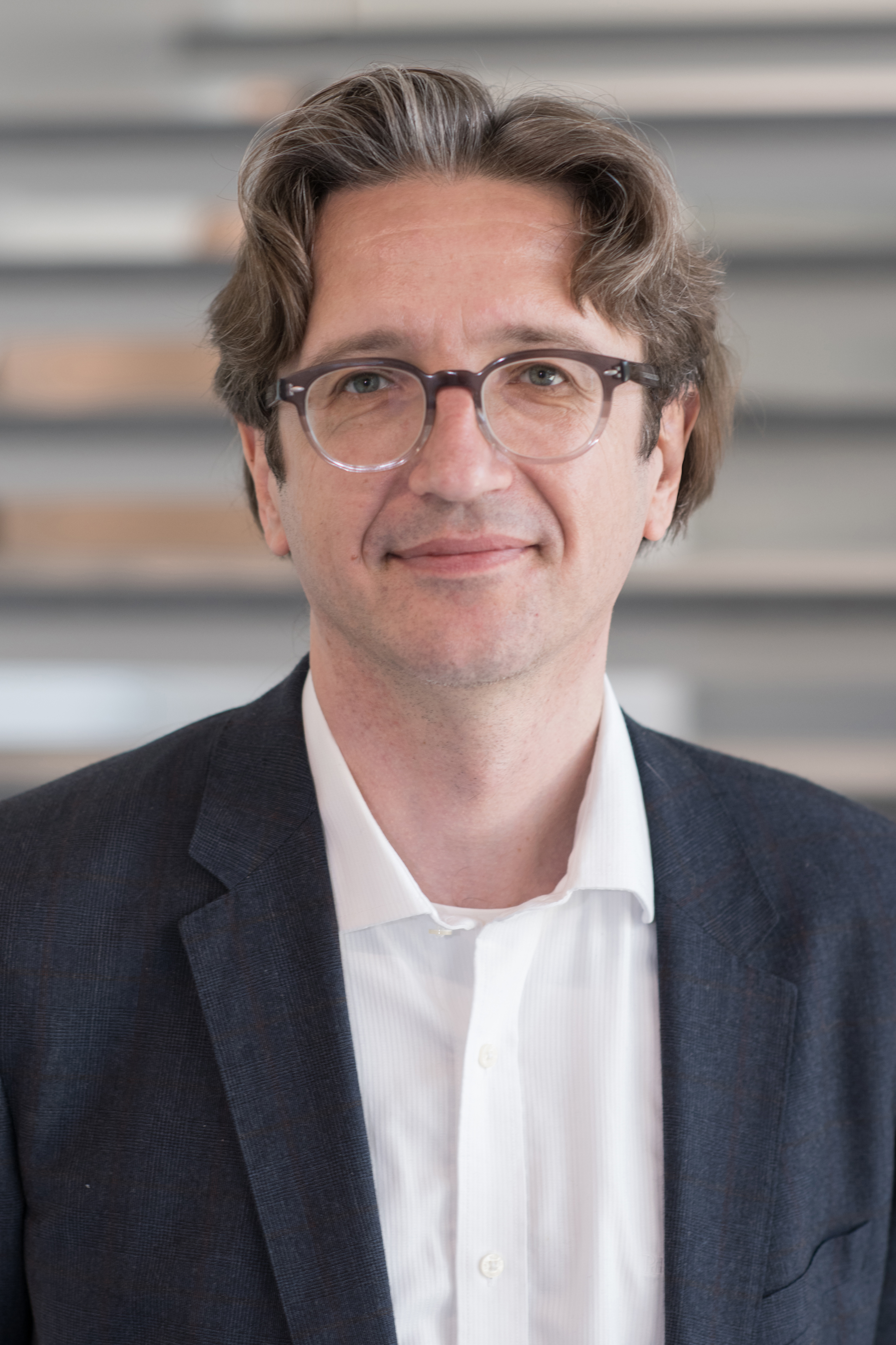 Portrait image of smiling man in suit with glasses and brown hair.