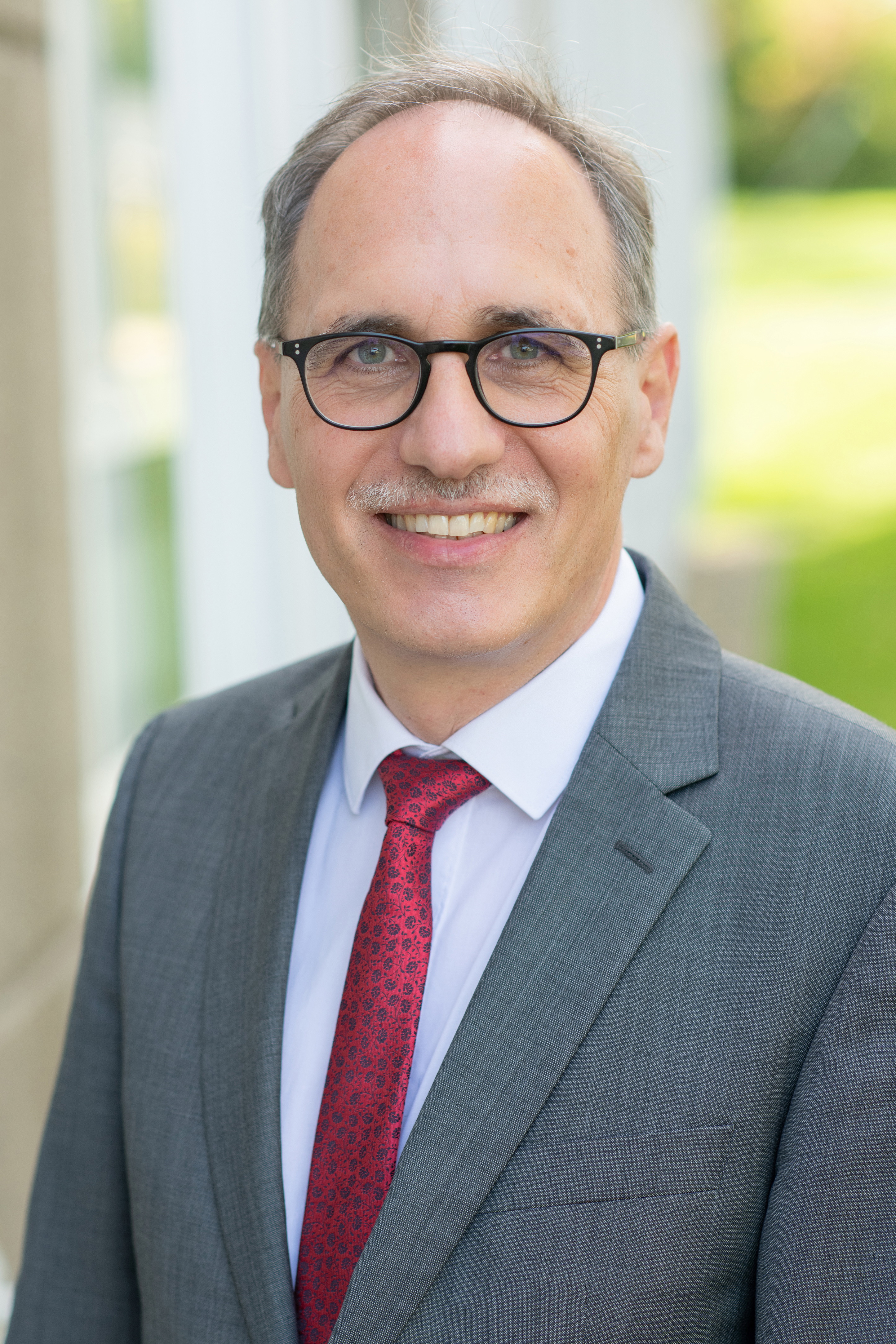 Portrait picture of man in gray suit with moustache and glasses.