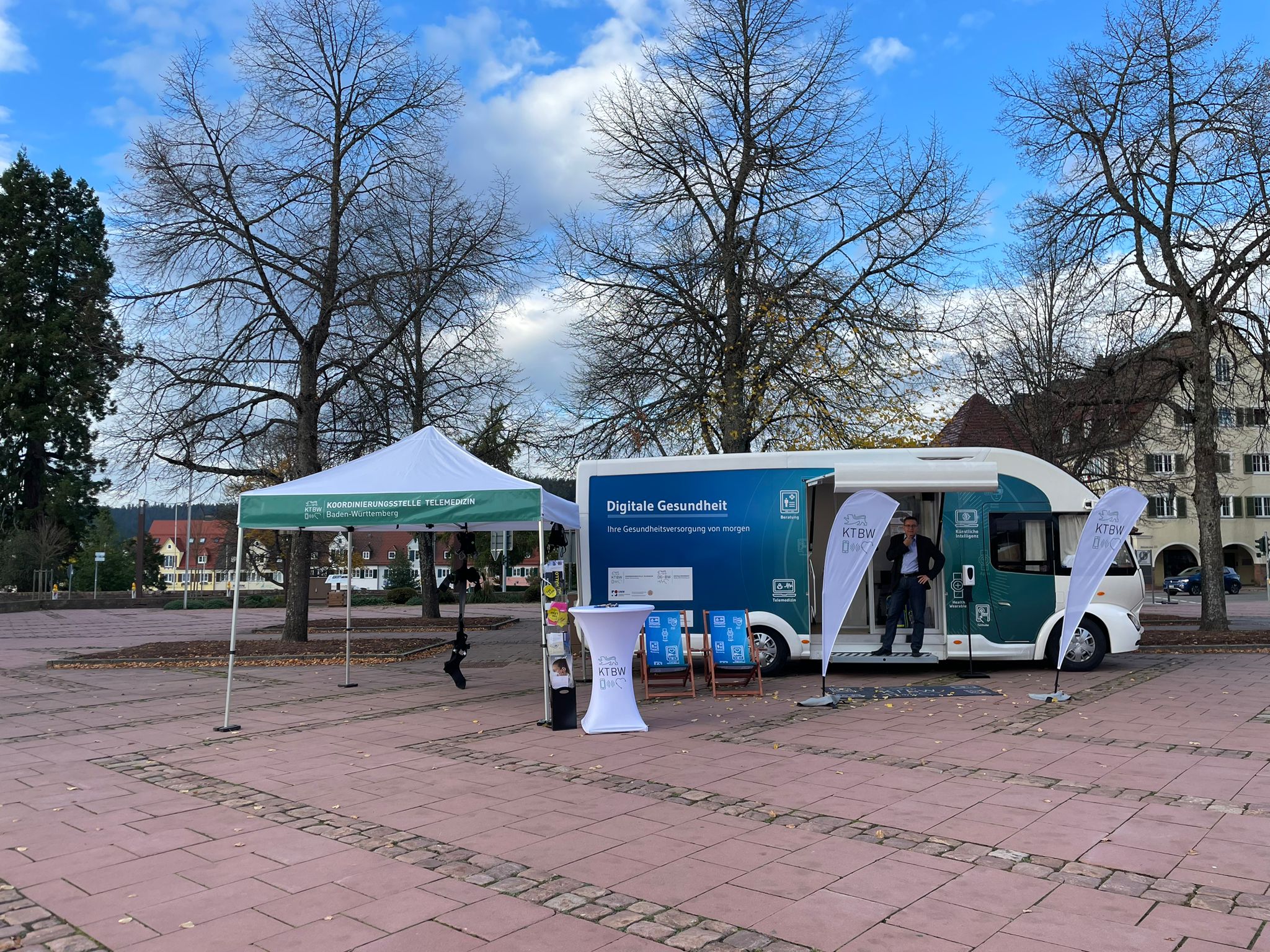 Der Truck steht vor Bäumen und blauem Himmel. Im Eingangsbereich der Trucks steht eine Person.