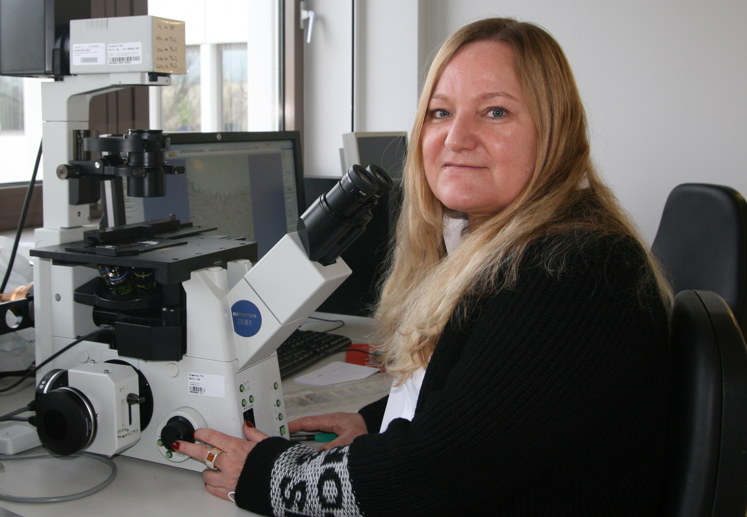 Eine Wissenschaftlerin sitzt an einem Lichtmikroskop.
