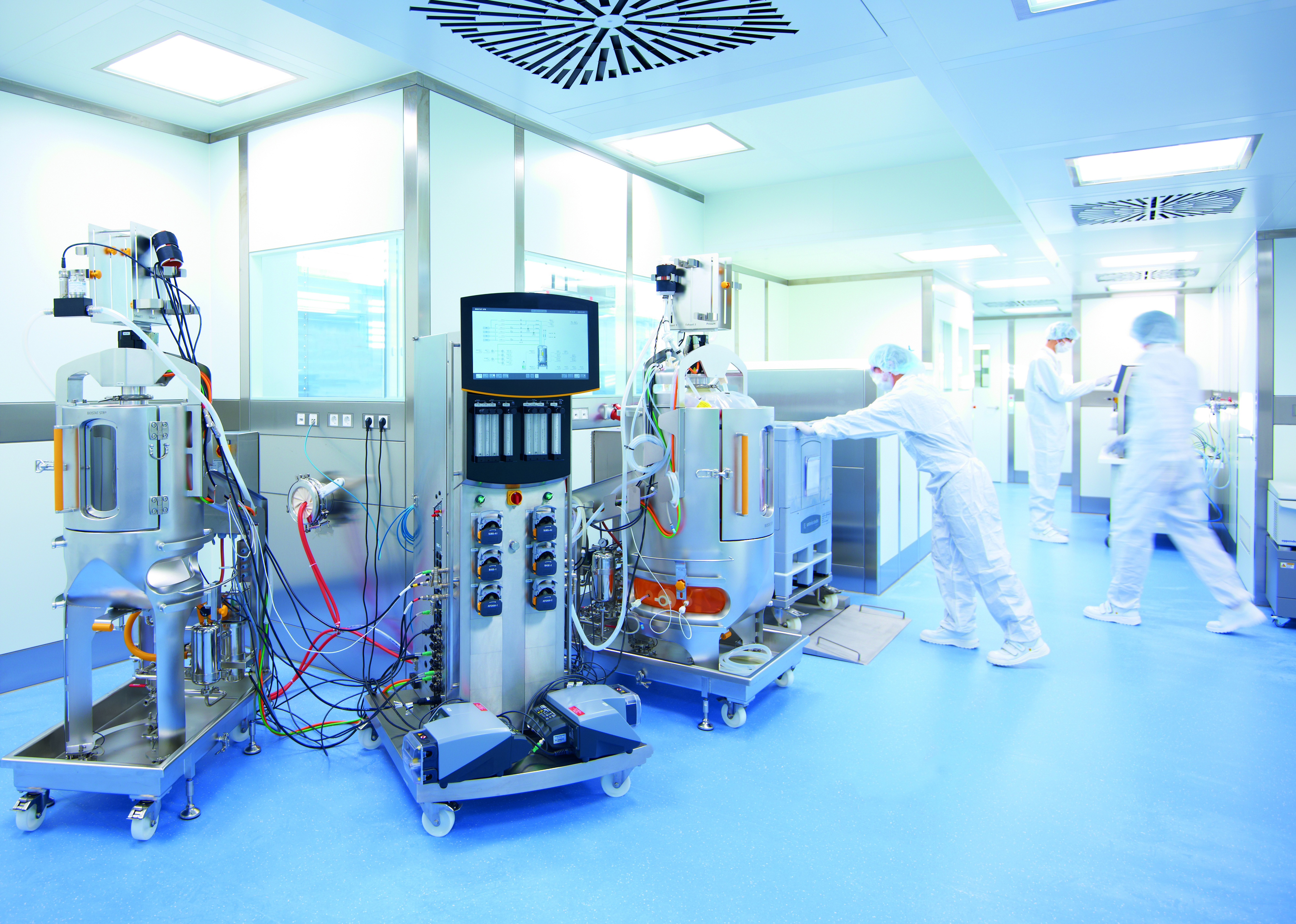 The photo shows a cleanroom with equipment used for downstream processing and some employees wearing GMP-compliant safety clothing.