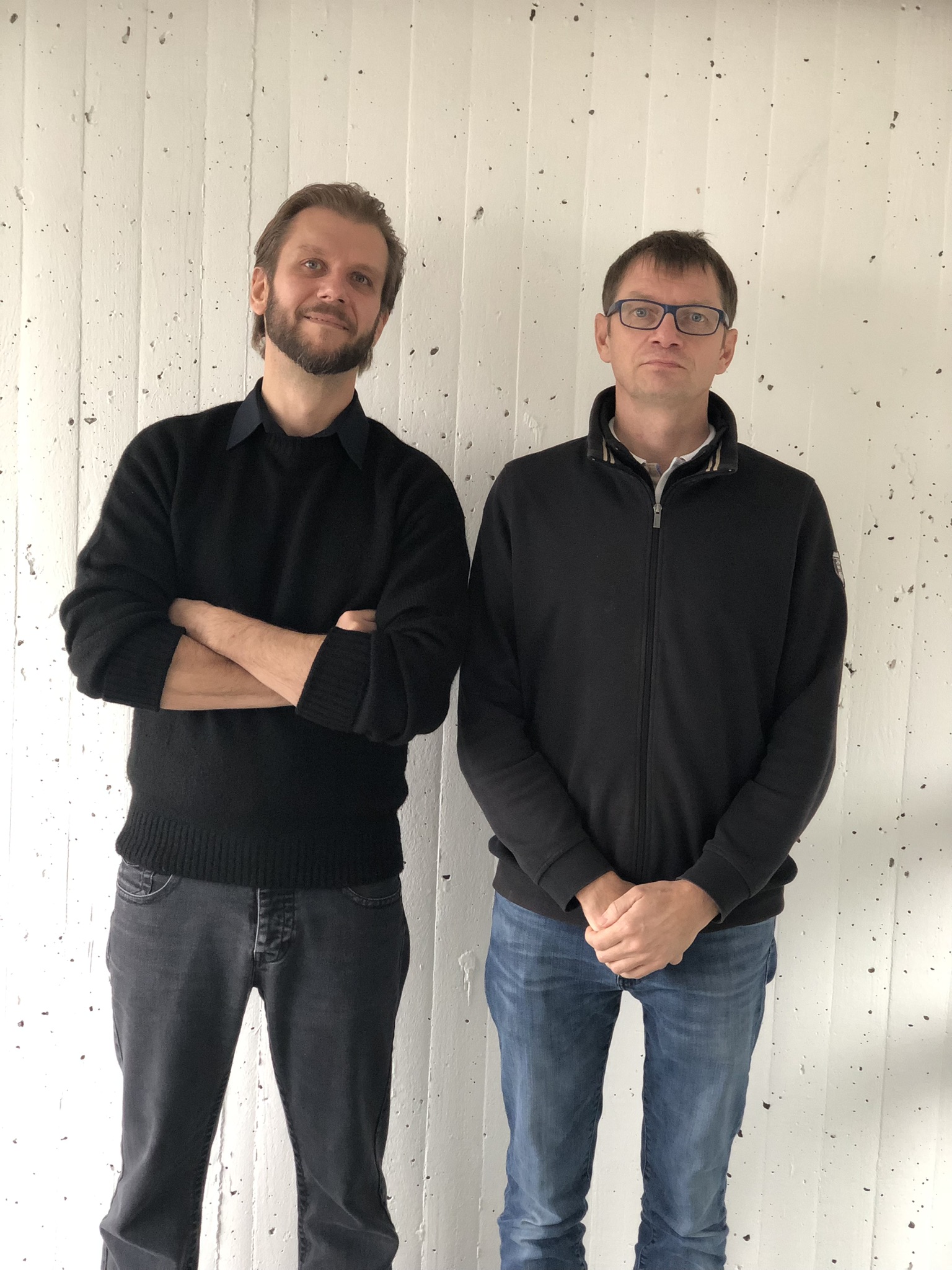 Two men standing in front of a bright wall.