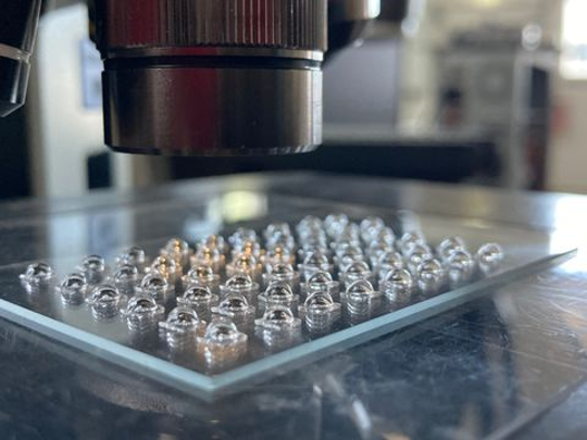 Rectangular glass plate with numerous convex, lens-shaped structures viewed under a microscope.
