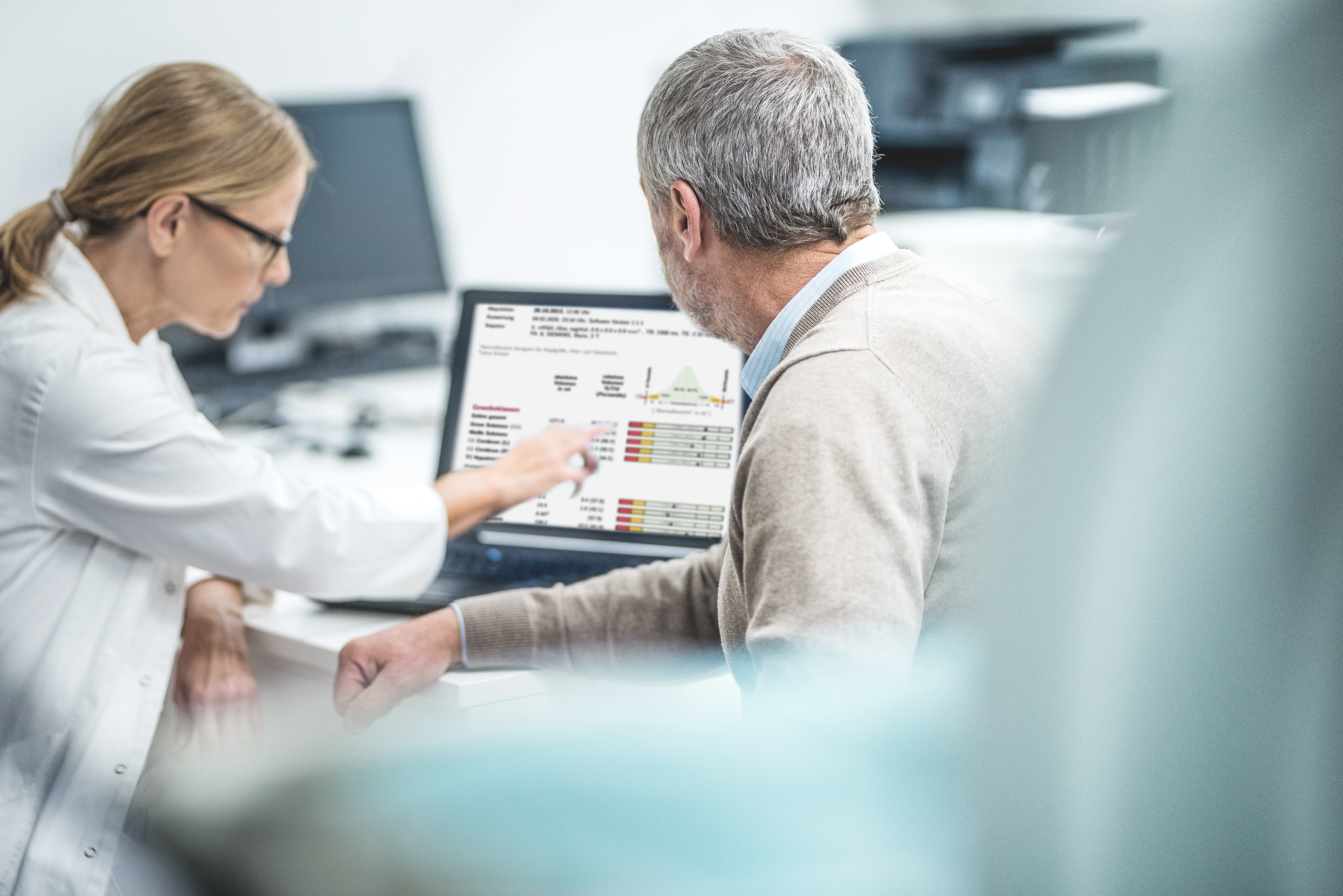 Eine Ärztin, die vor einem Computer mit Schaubildern auf dem Bildschirm sitzt und ihrem Patienten die Auswertung erklärt.