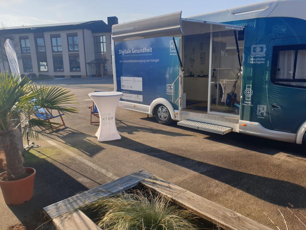 Der Truck steht an einem sonnigen Tag auf einem Parkplatz. Im Hintergrund sieht man ein Gebäude.