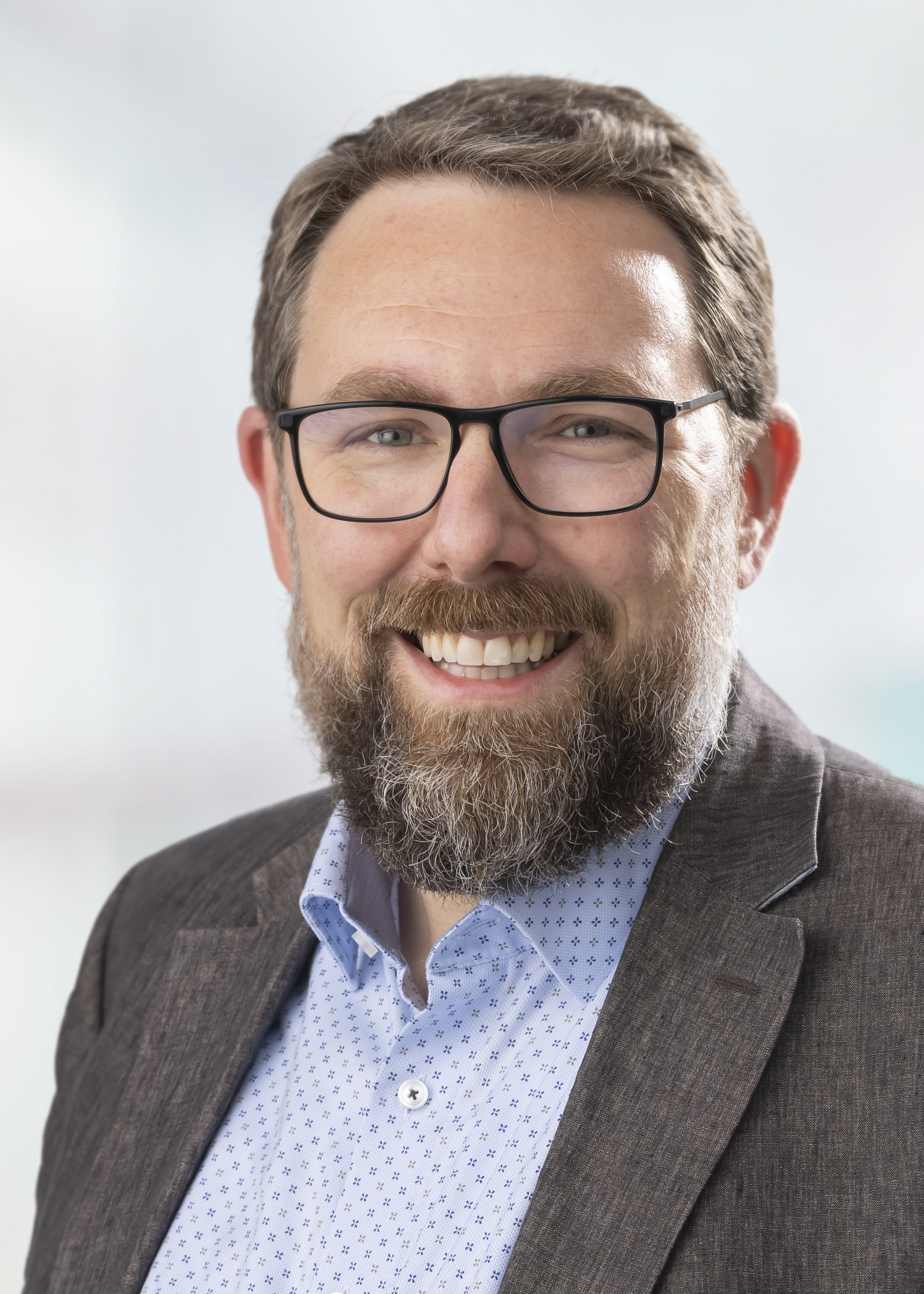 Portrait of a friendly smiling man with ash blond hair, beard and glasses.