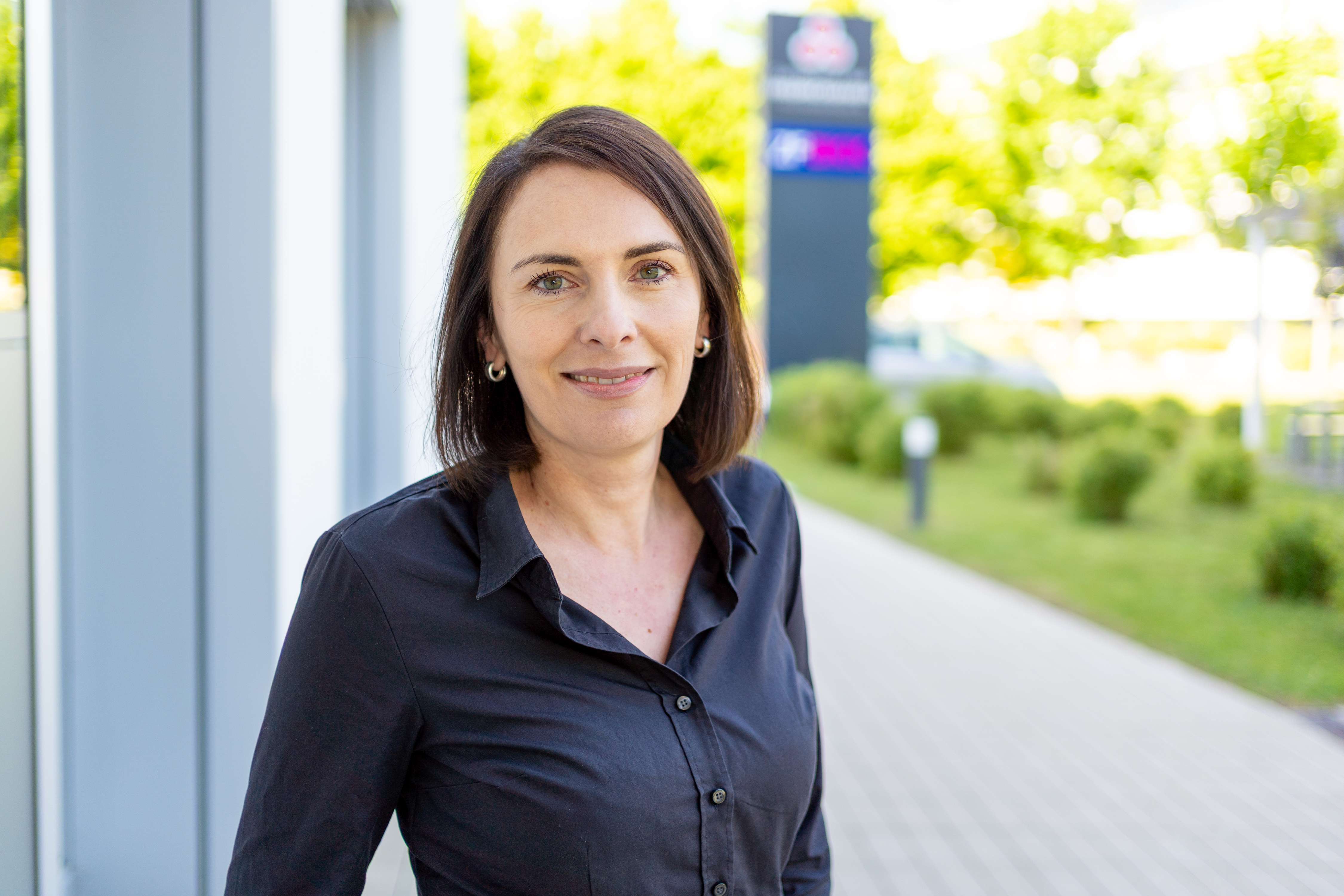 eine Frau in einer schwarzen Bluse steht außerhalb eines Gebäudes.