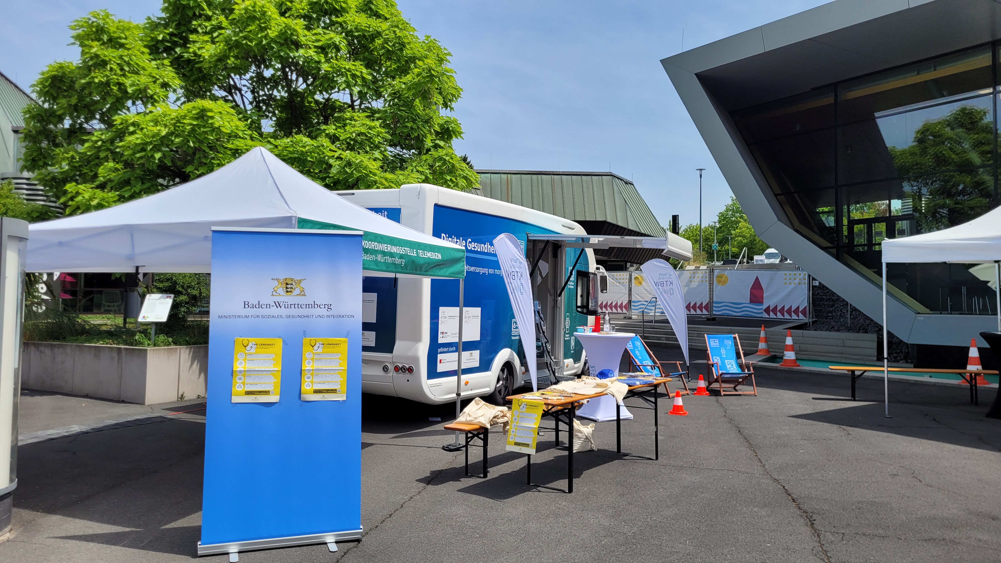 Der Truck steht vor einem Gebäude. Es ist ein Aufsteller des Ministeriums für Soziales, Gesundheit und Integration Baden-Württemberg zu sehen, auf welchem auf die "The Ländarzt" Initiative hingewiesen wird.