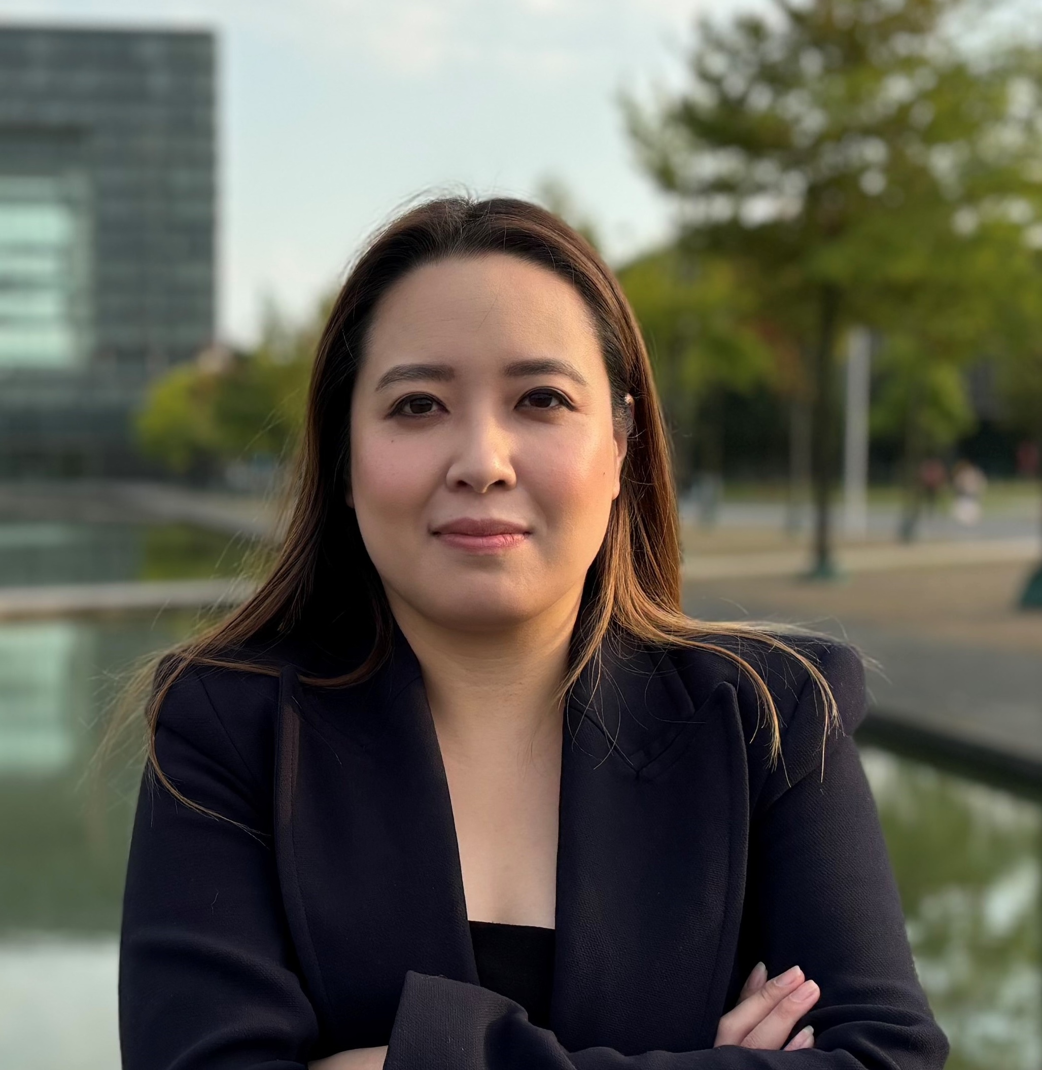 Dr Anh Mattick, a woman in a blazer, looks seriously into the camera against the blurred background of a modern building on the waterfront.