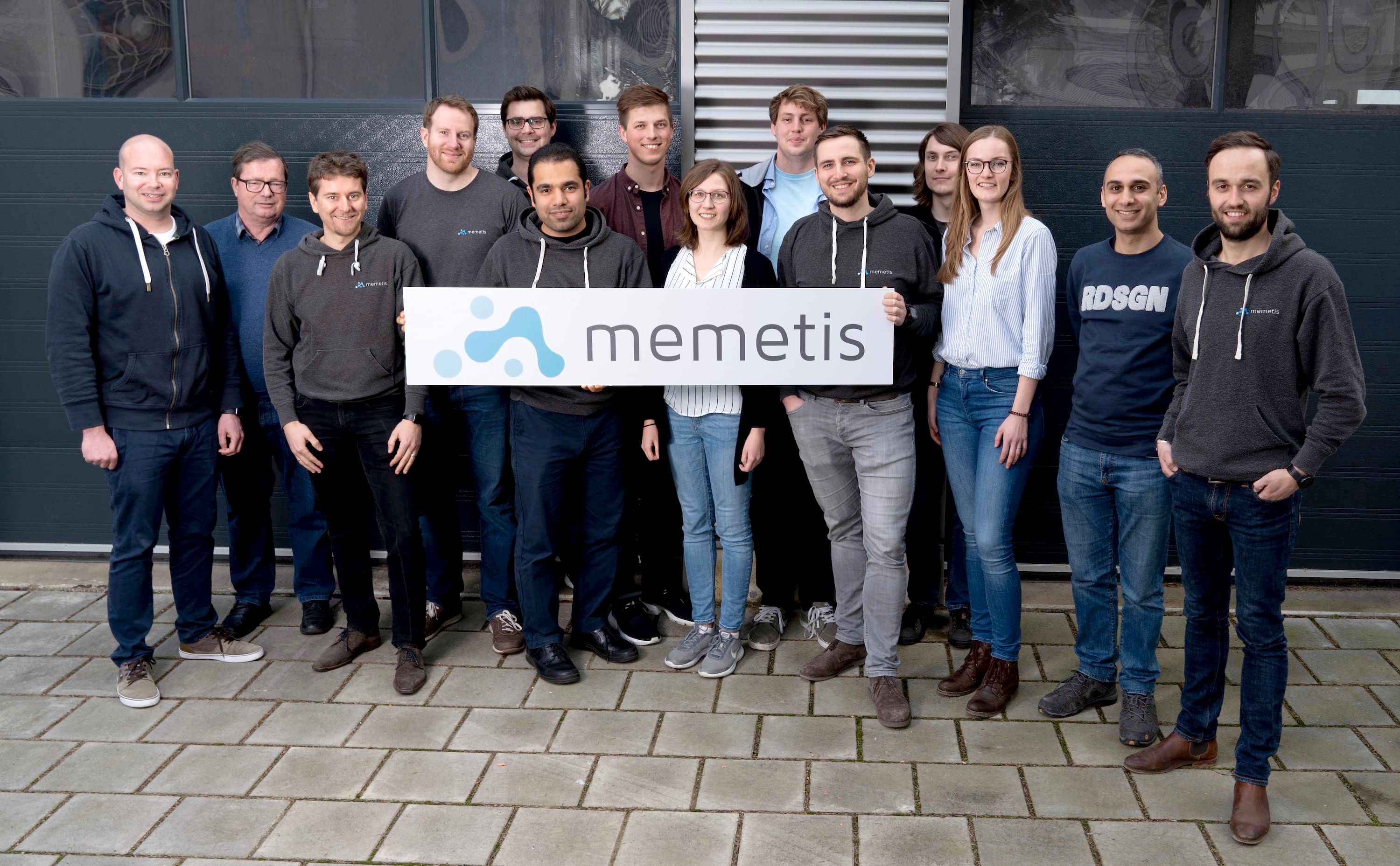 Team mit 14 Personen halten ein Firmenschild mit der Aufschrift memetis in der Hand