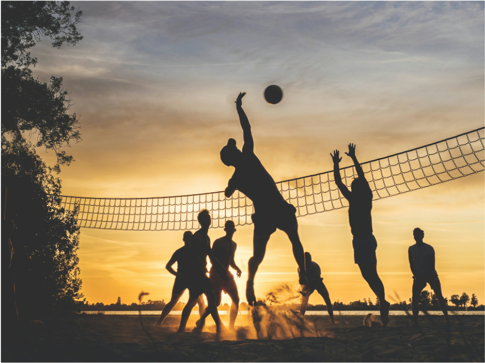 A group of people playing volleyball during sunset.