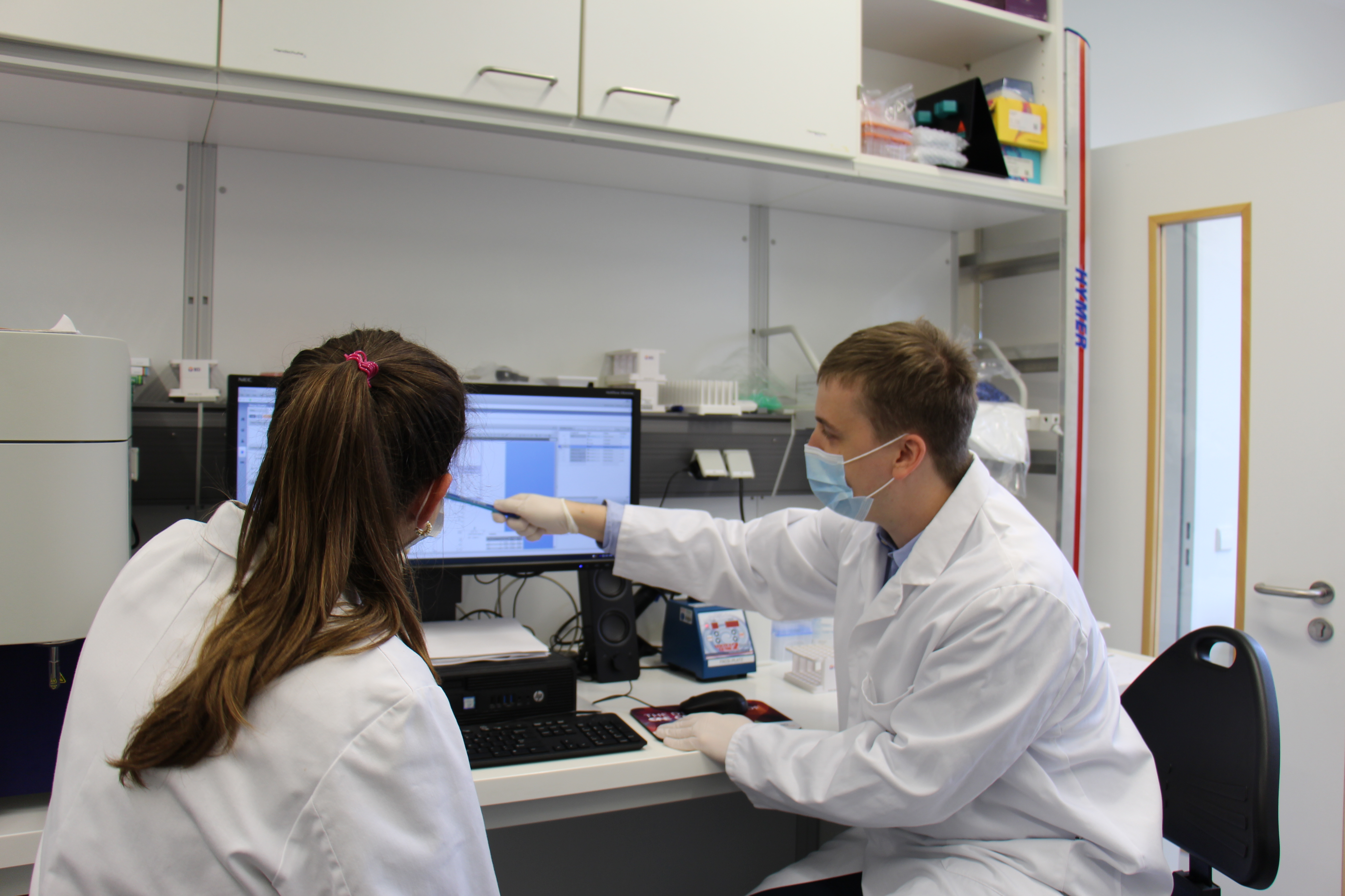 The doctor with face mask and lab coat with a doctoral student in front of an evaluation computer.