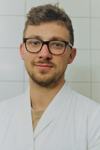 Portrait photo of a young man wearing glasses and a lab coat.