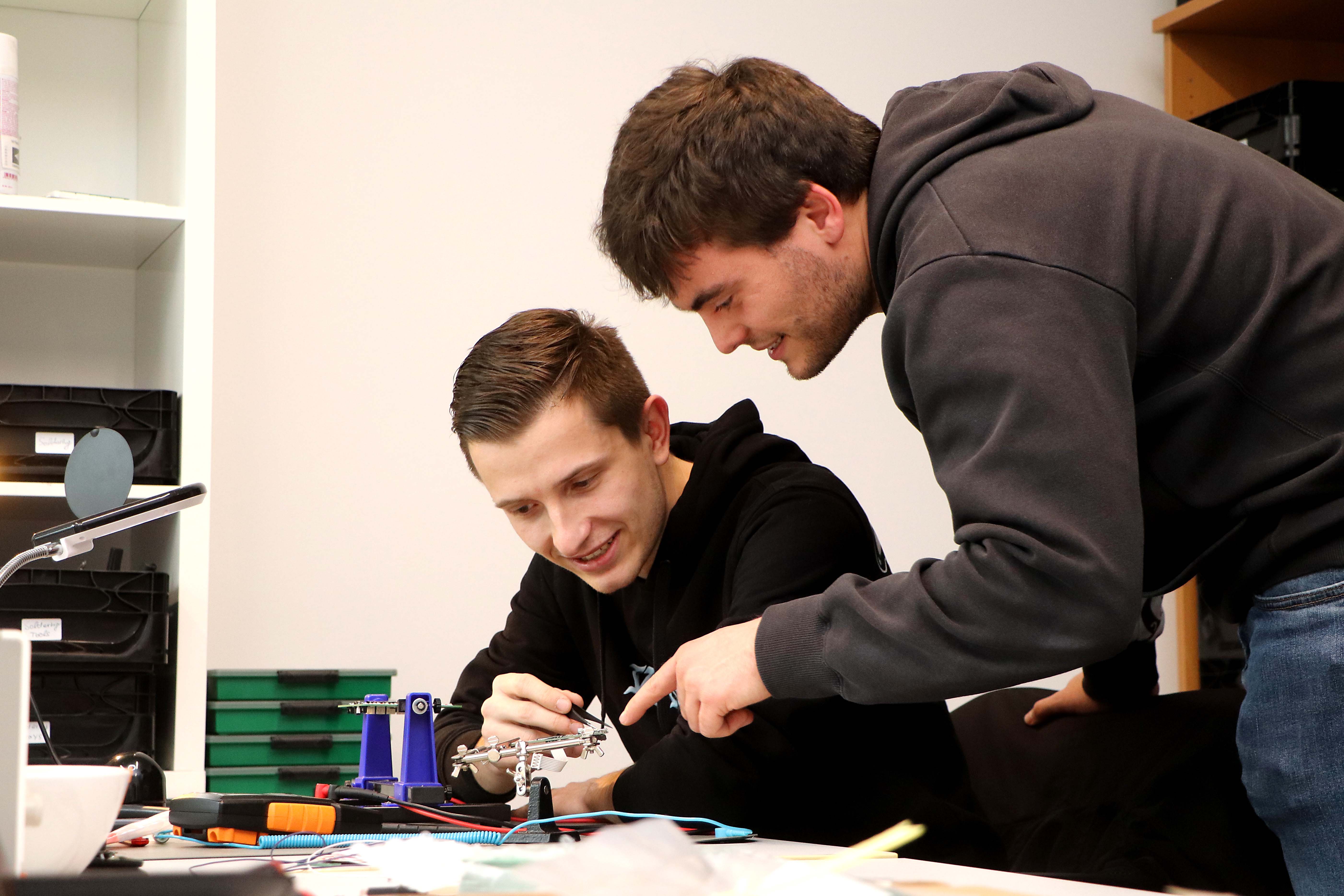 Two employees can be seen bending over and discussing a technical device in the workshop.