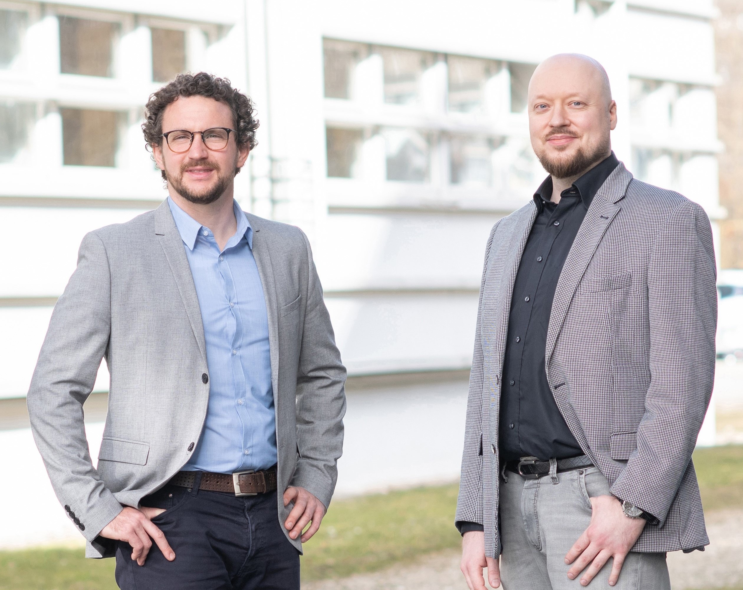 Die beiden Experten stehend vor einem weißen Geschäftsgebäude.