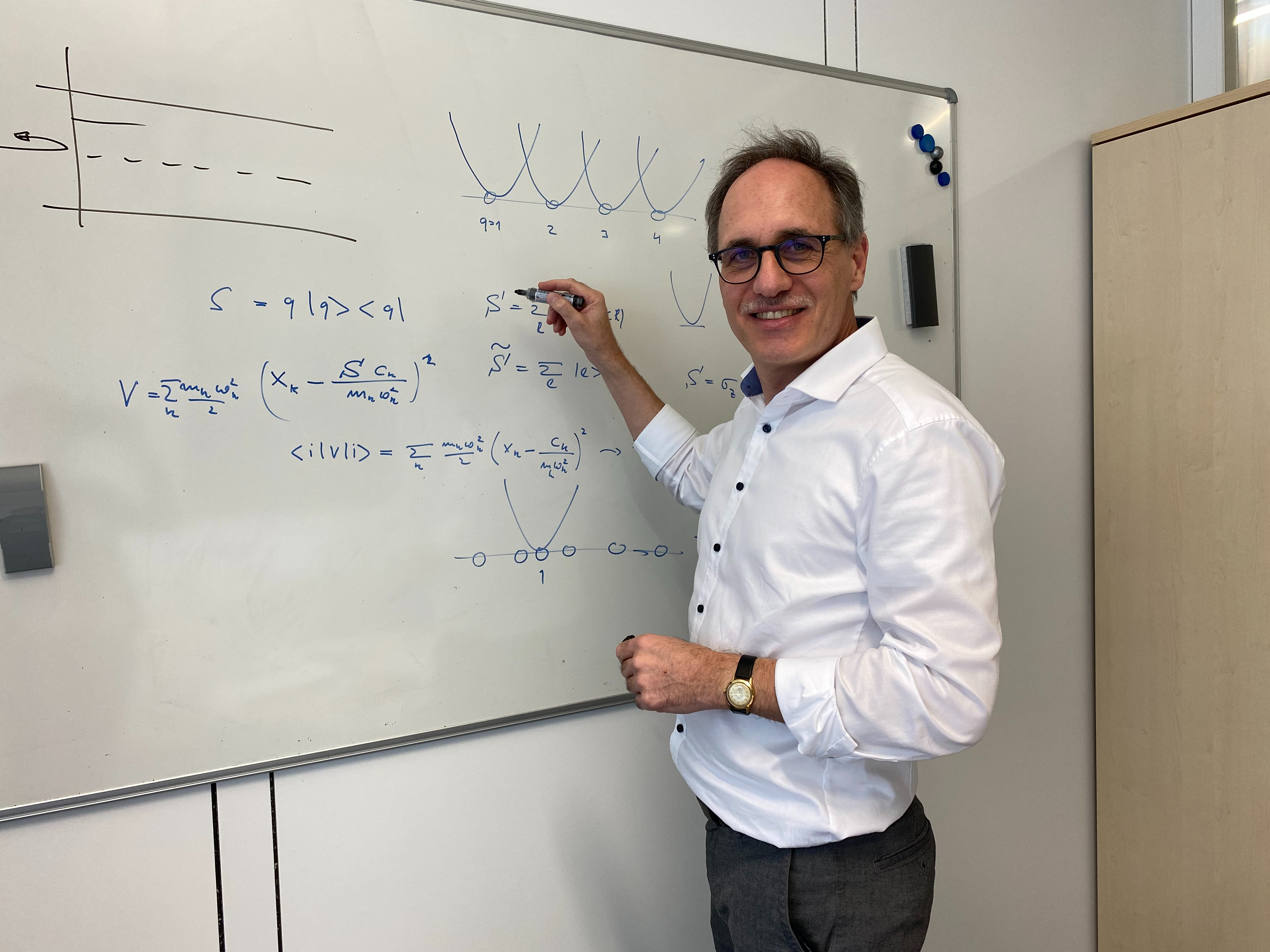 Dozent im weißen Hemd beschriftet ein White-Board mit physikalischen Gleichungen. Der Dozent ist Prof. Ankerhold der Universität Ulm.