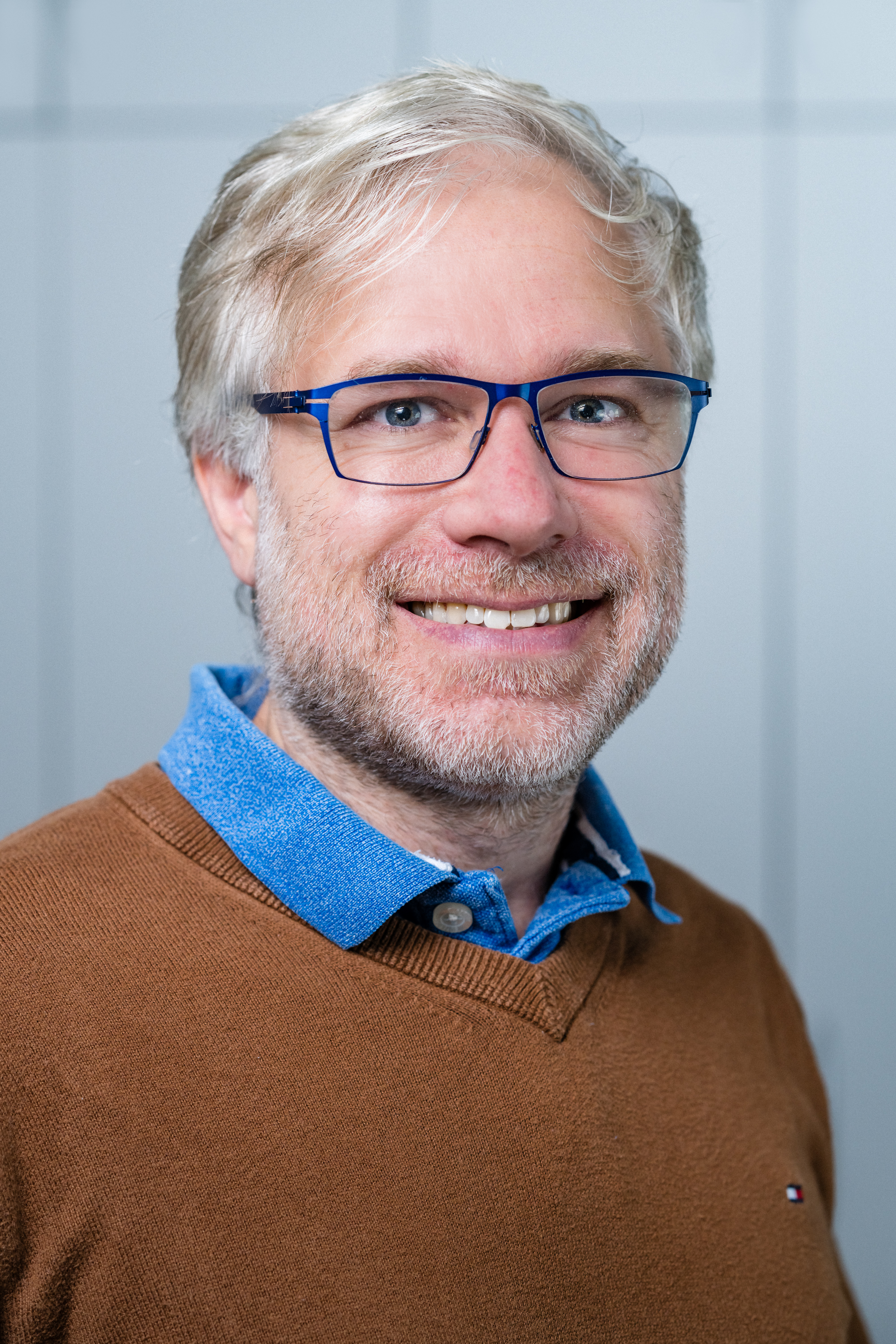 Porträt des Wissenschaftlers in braunem Pullover vor weißer Wand.