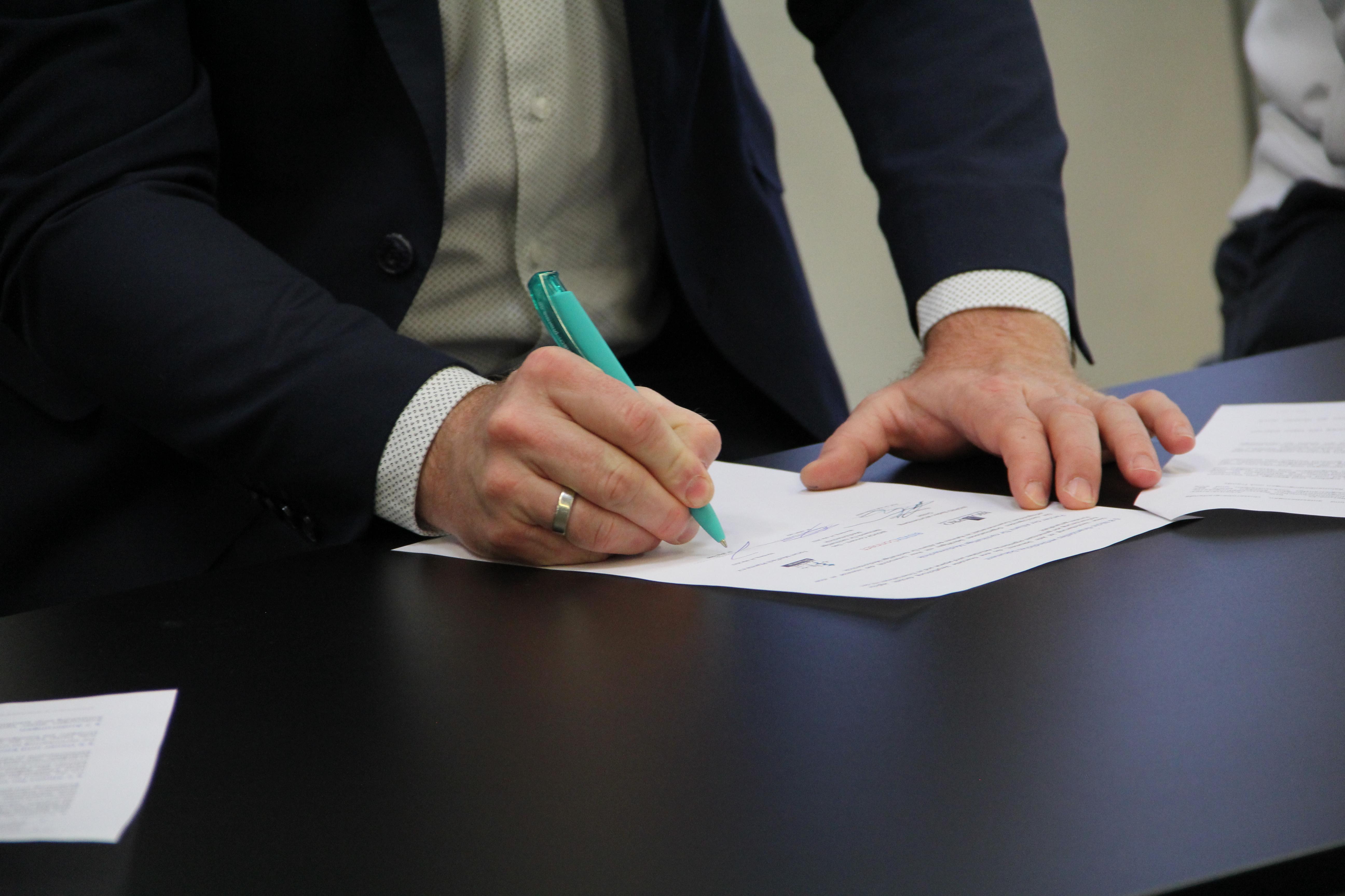 Eine Person die mit einem grünen Stift auf ein Dokument unterschreibt