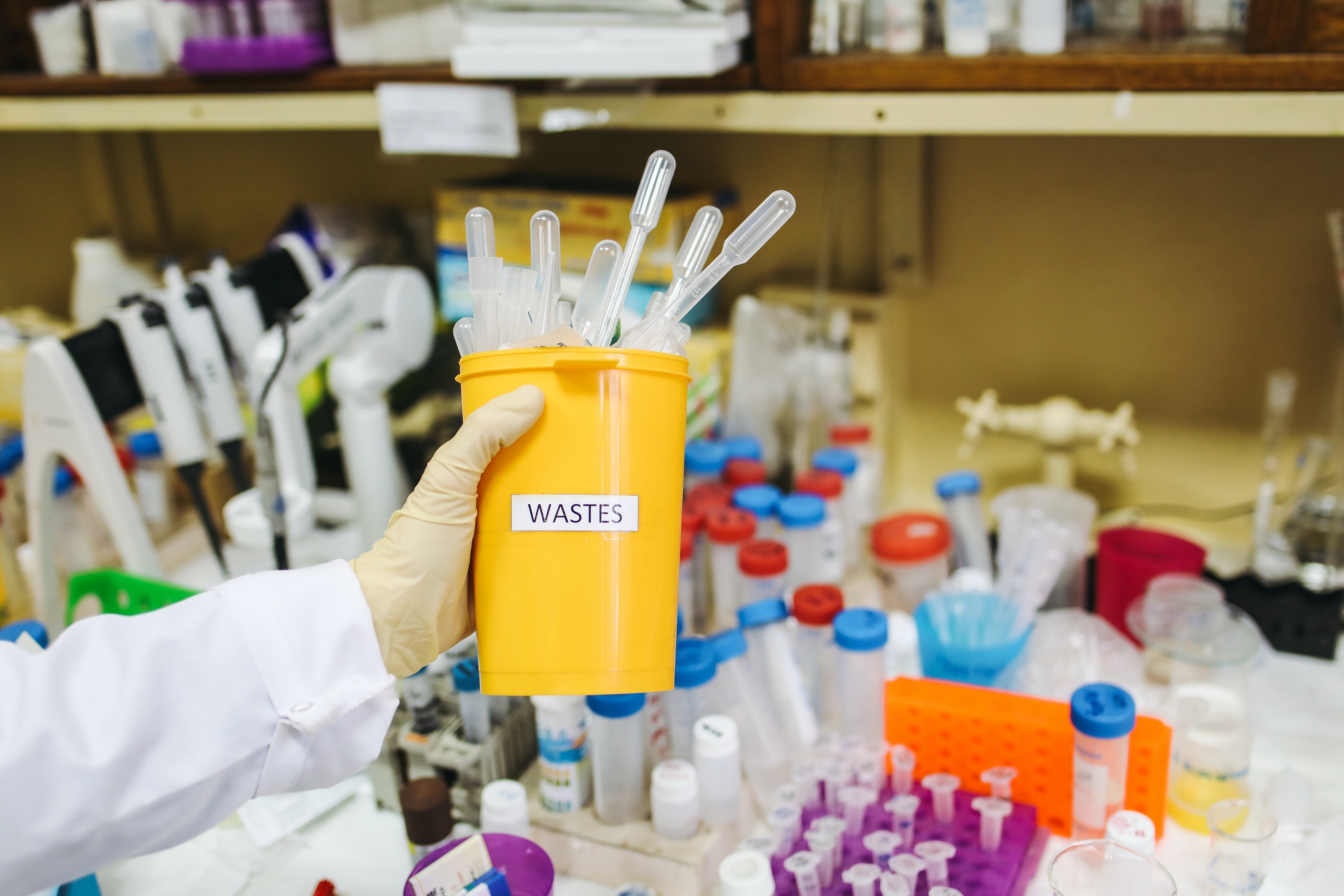 Glove hand holding yellow container with plastic laboratory waste.