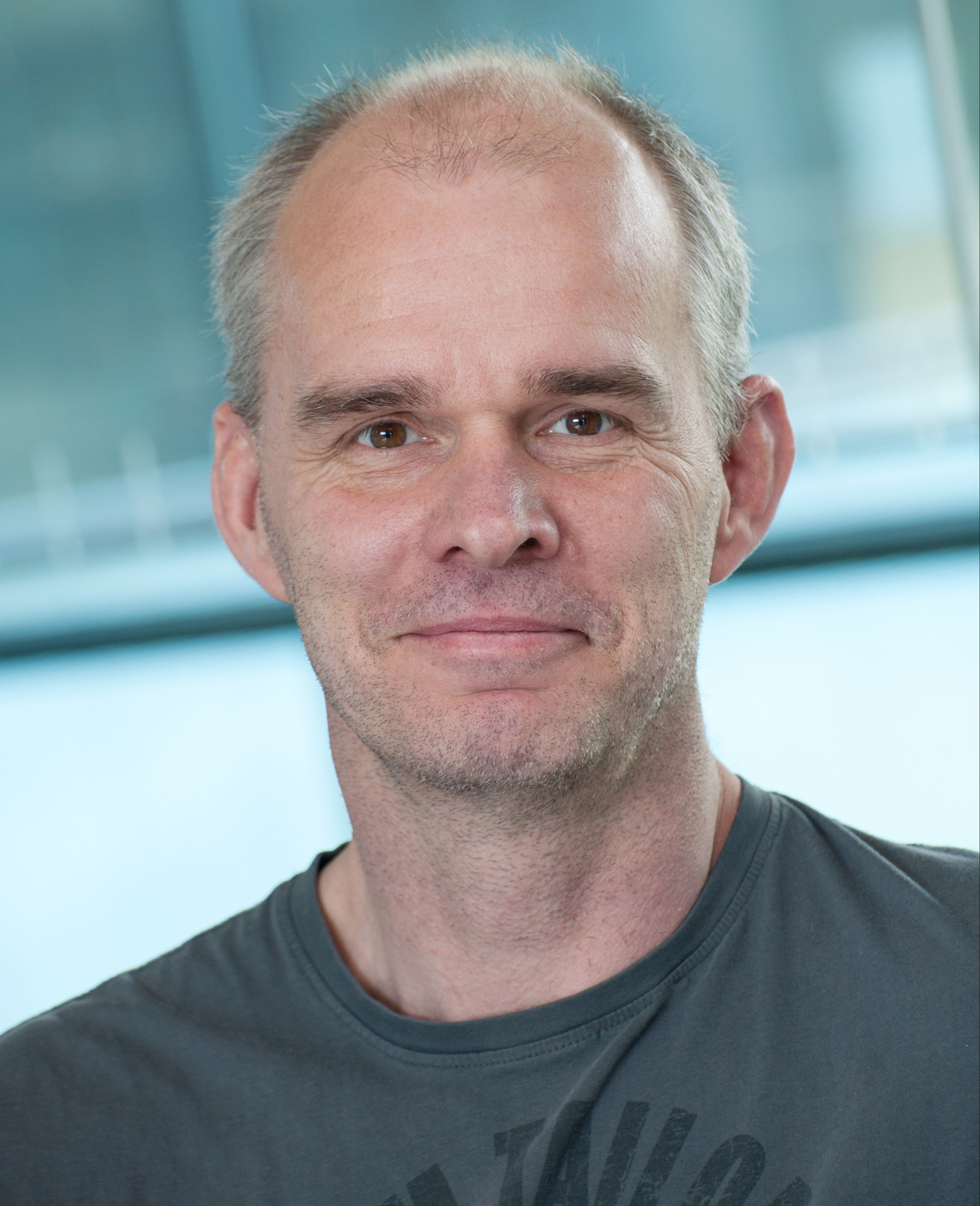 You can see a man with a three-day beard and short hair looking friendly into the camera.