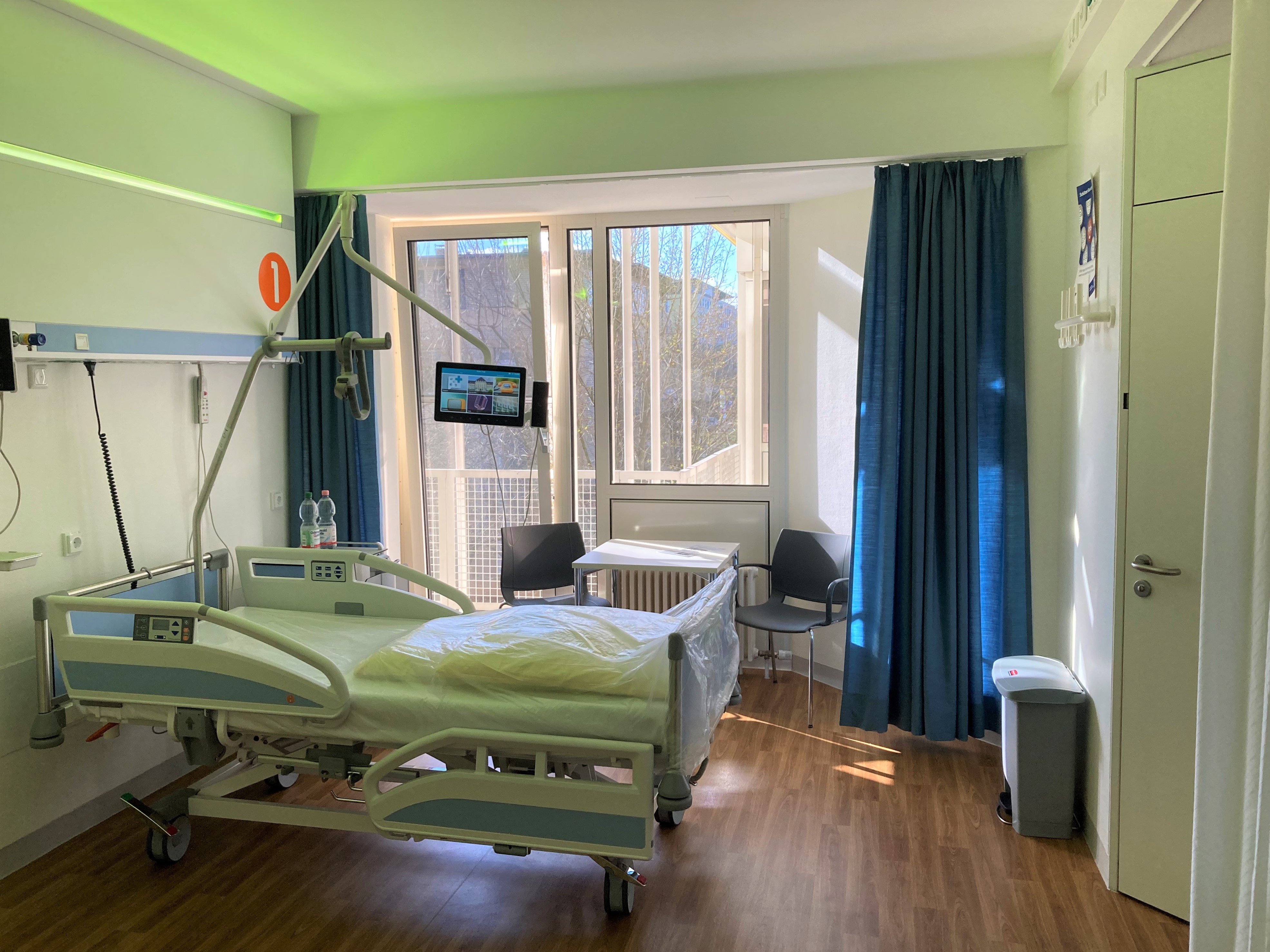 The photo shows a modern hospital room with a nursing bed.