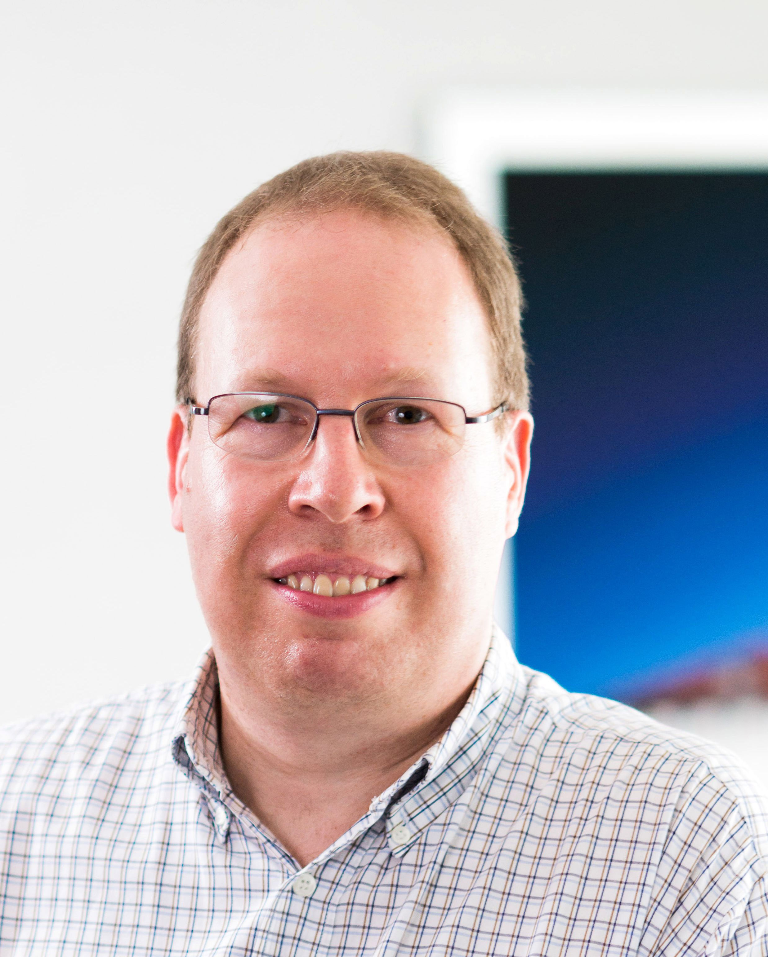 A man with glasses and a checked shirt can be seen smiling friendly into the camera.