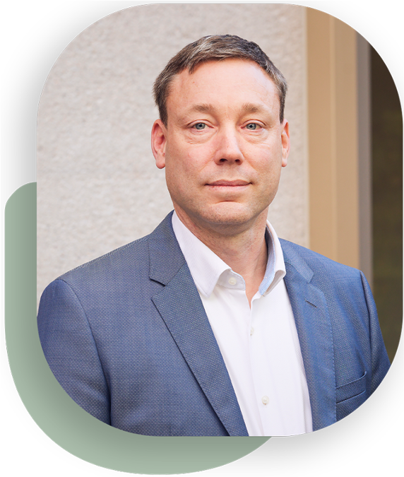 A man with short hair in a blue suit looks into the camera.