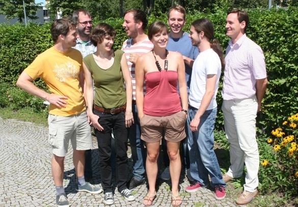Zu sehen ist eine Gruppe von acht Personen vor einer grünen Hecke.