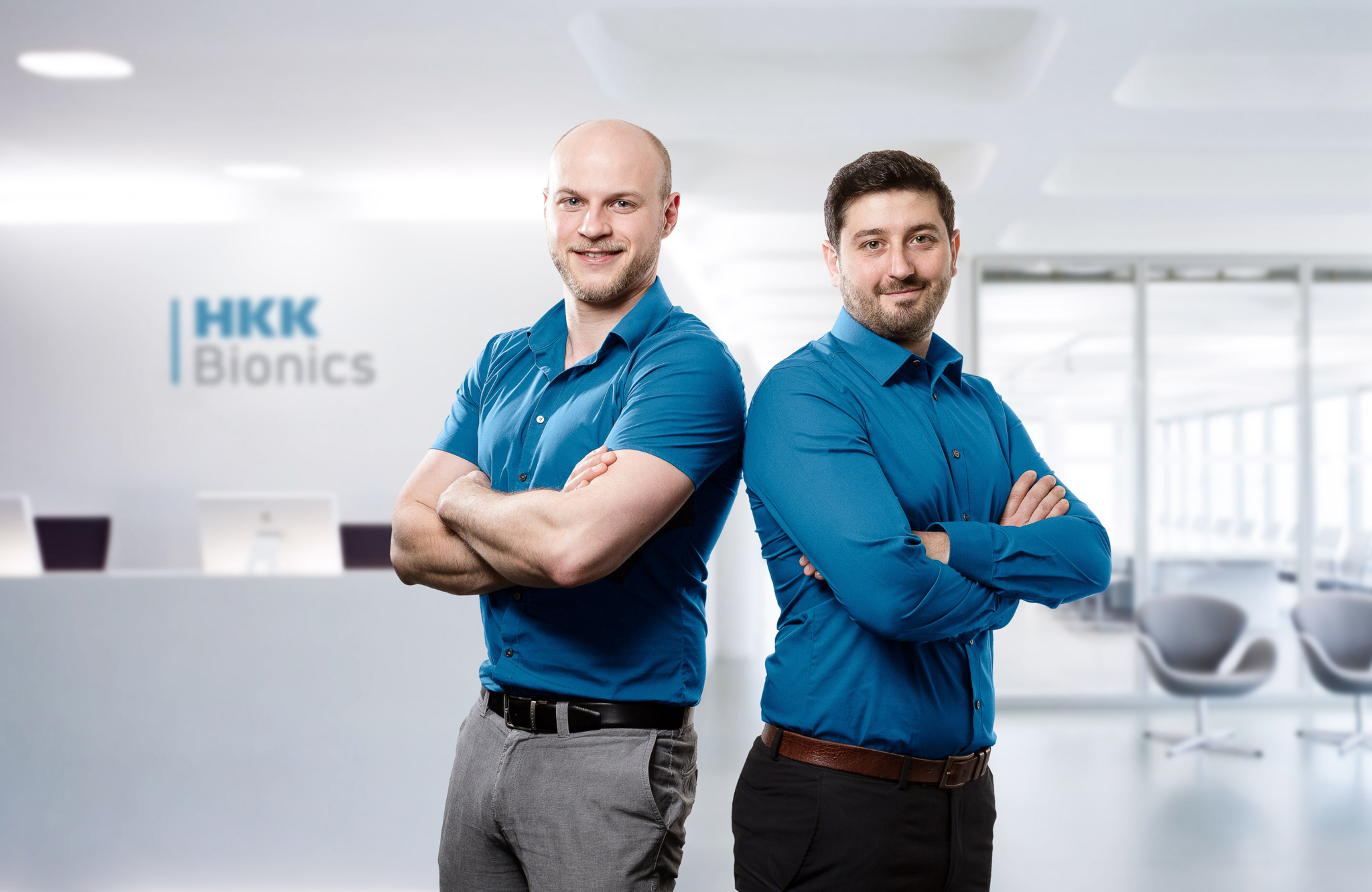 Das Bild zeigt die beiden Unternehmensgründer Dominik Hepp und Tobias Knobloch sowie im Hintergrund das Emblem des Spin-off HKK Bionics.