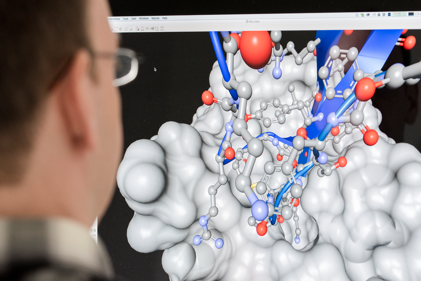 The head of a scientist in front of a computer screen showing a molecule model.