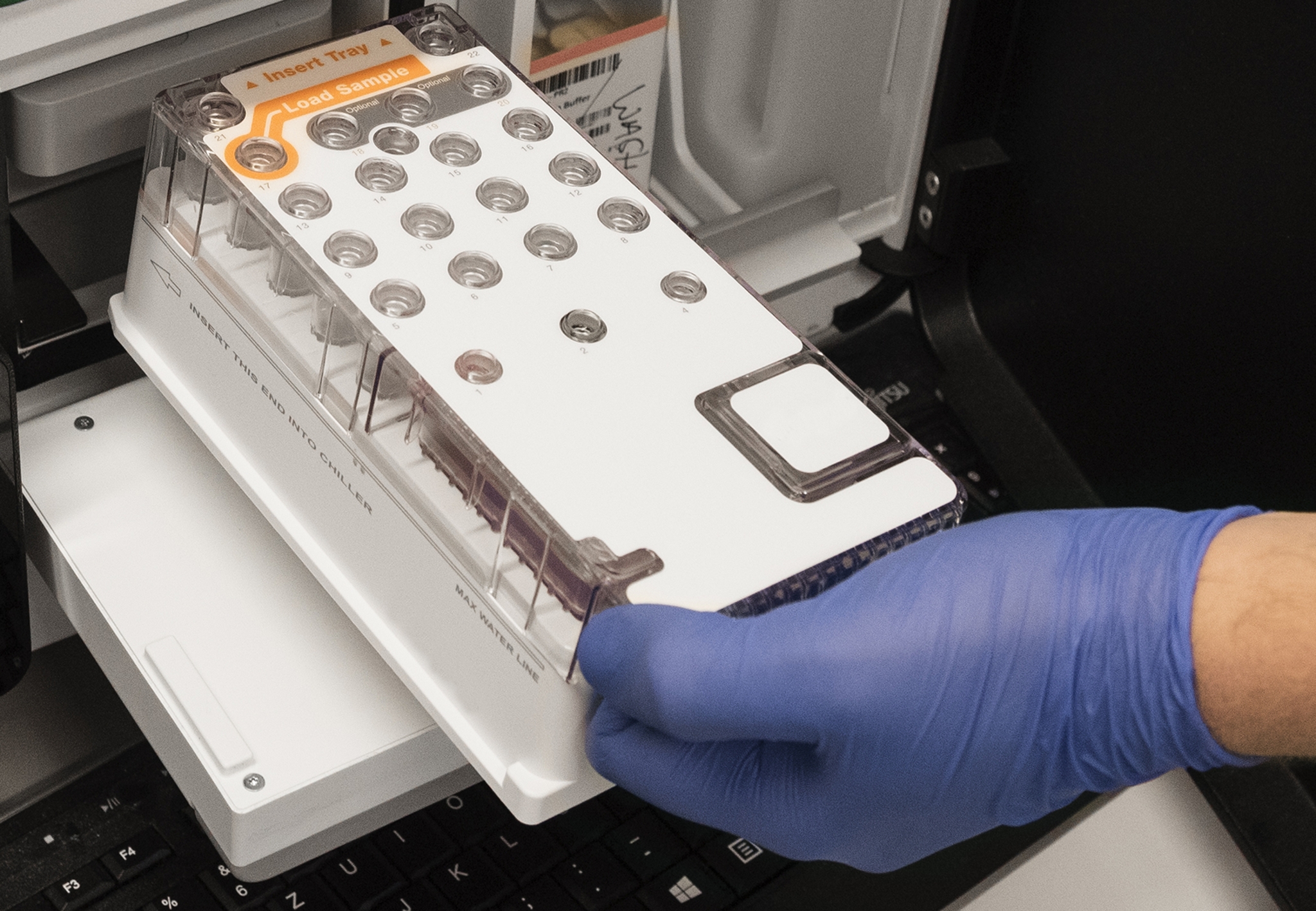 The photo shows a sample plate being inserted into a sequencing apparatus.