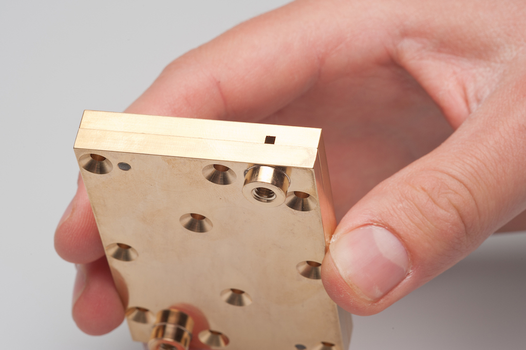 The photo shows the small rectangular device developed by chemist Prof. Mizaikoff from Ulm. The photo shows a golden plate with several openings, both rectangular and round ones, and cylinder-shaped ones. The substrate-integrated hollow waveguide can be u