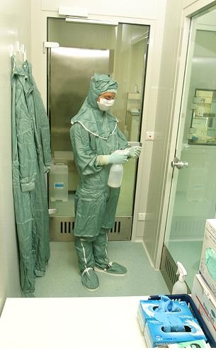 Zu sehen ist eine in hellblaue Schutzkleidung und Mundschutz gekleidete Person in einem Laborraum.
