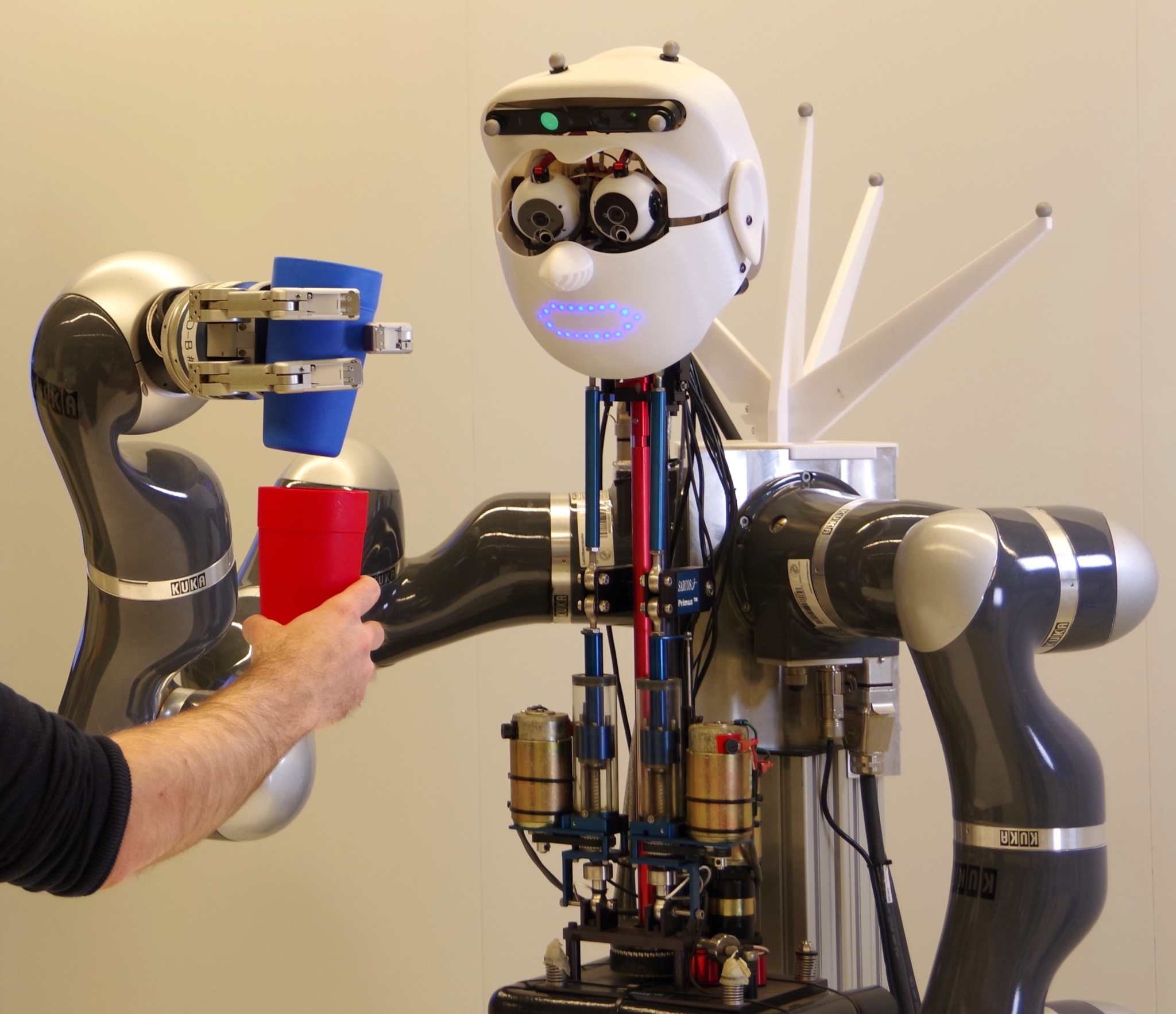 The robot Apollo in the laboratory: it is holding a blue cup and is offered a red cup by a human hand.