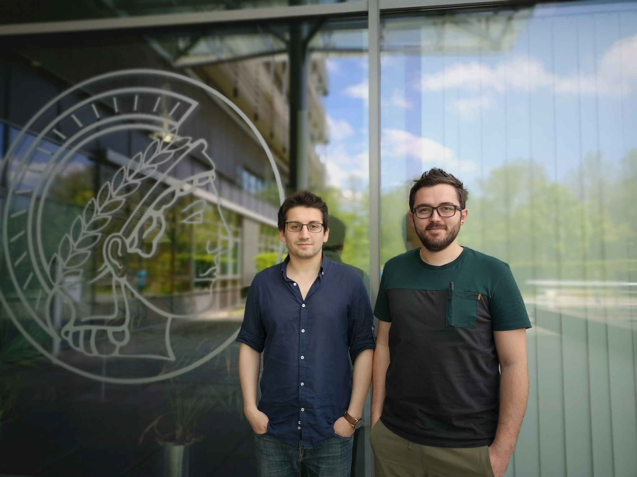 The two scientists standing in front of a door with a Max Planck logo.