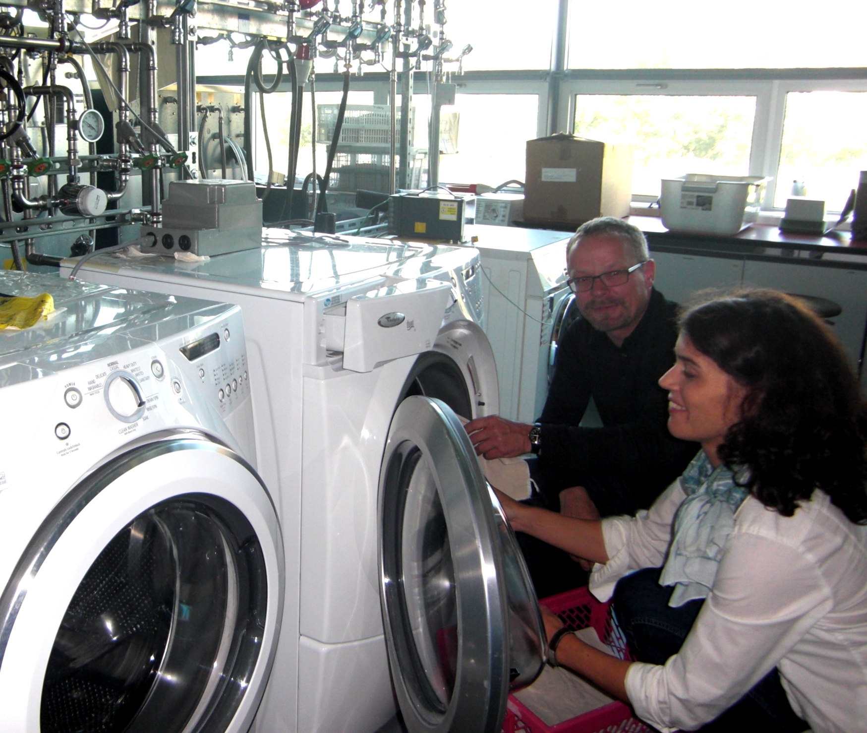 Daniel Fäh, Geschäftsführer der Empa Testmaterials AG, mit Caroline Amberg, Projektleiterin für Mikrobiologie des Unternehmens im Waschraum vor einer Waschmaschine hockend beim Beladen des Geräts mit Testgewebe.