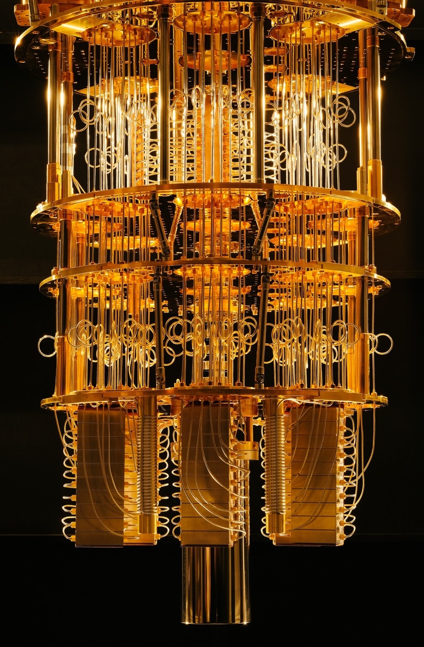Foto des 50-Qubit-Quantencomputers von IBM im IBM Q lab in Yorktown Heights, New York mitsamt Kühlvorrichtung. Er ist auf dem Foto so angeleuchtet, dass er wie ein Kronleuchter in gelb-orangenem Licht wirkt.