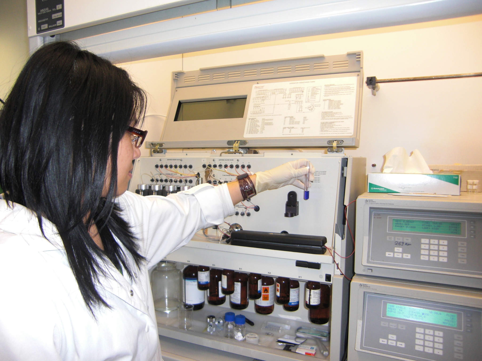 Scientist in the laboratory of Przybylski's reserach group at the University of Constance holding a test tube in her hand and standing in front of an analysis device.